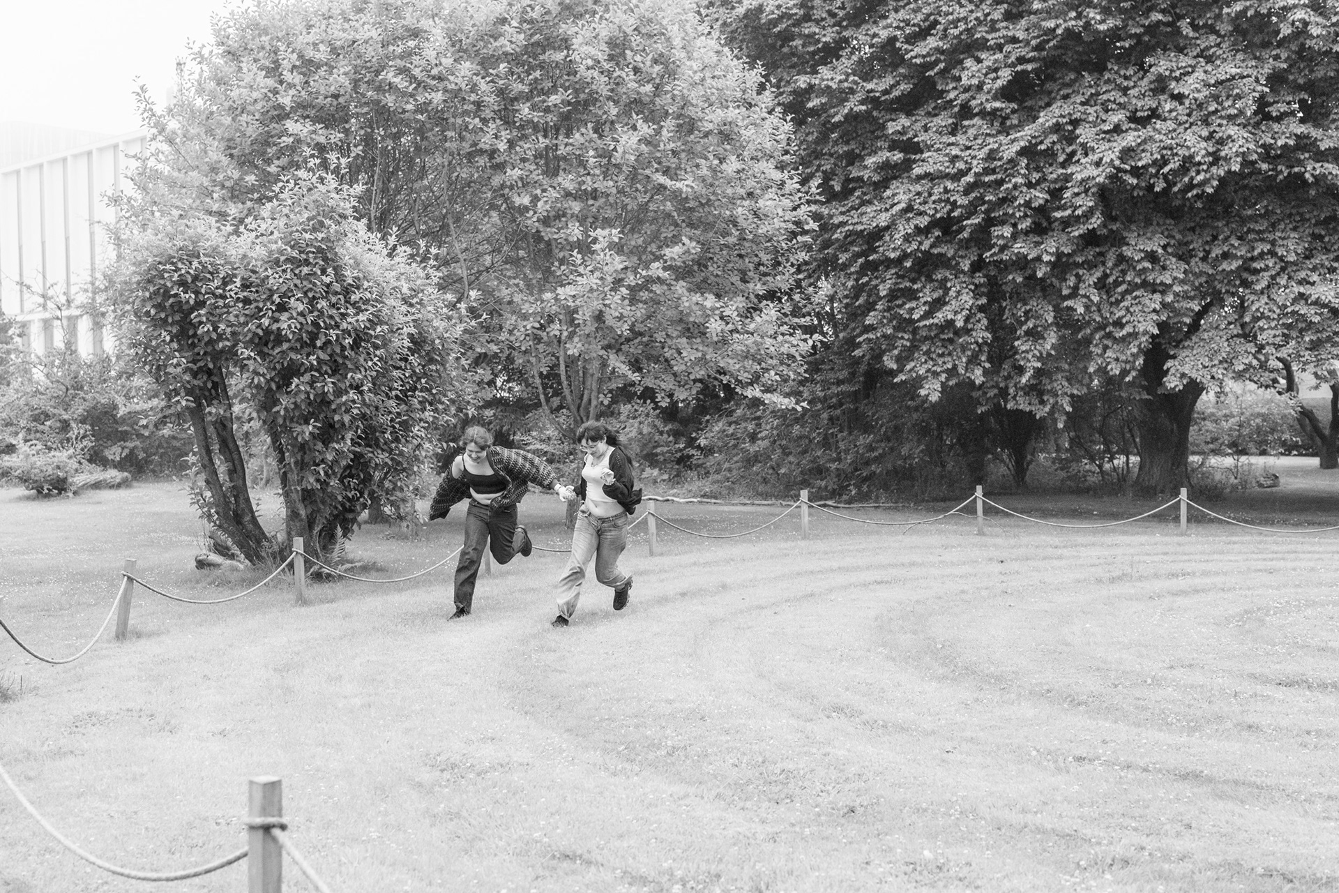 In this black and white photo by Aberdeen photographer, Sarah from Windswept Stories, a young couple hold hands and laugh as they run around a spiral mown into a lawn. Their cardigans fly out behind them.