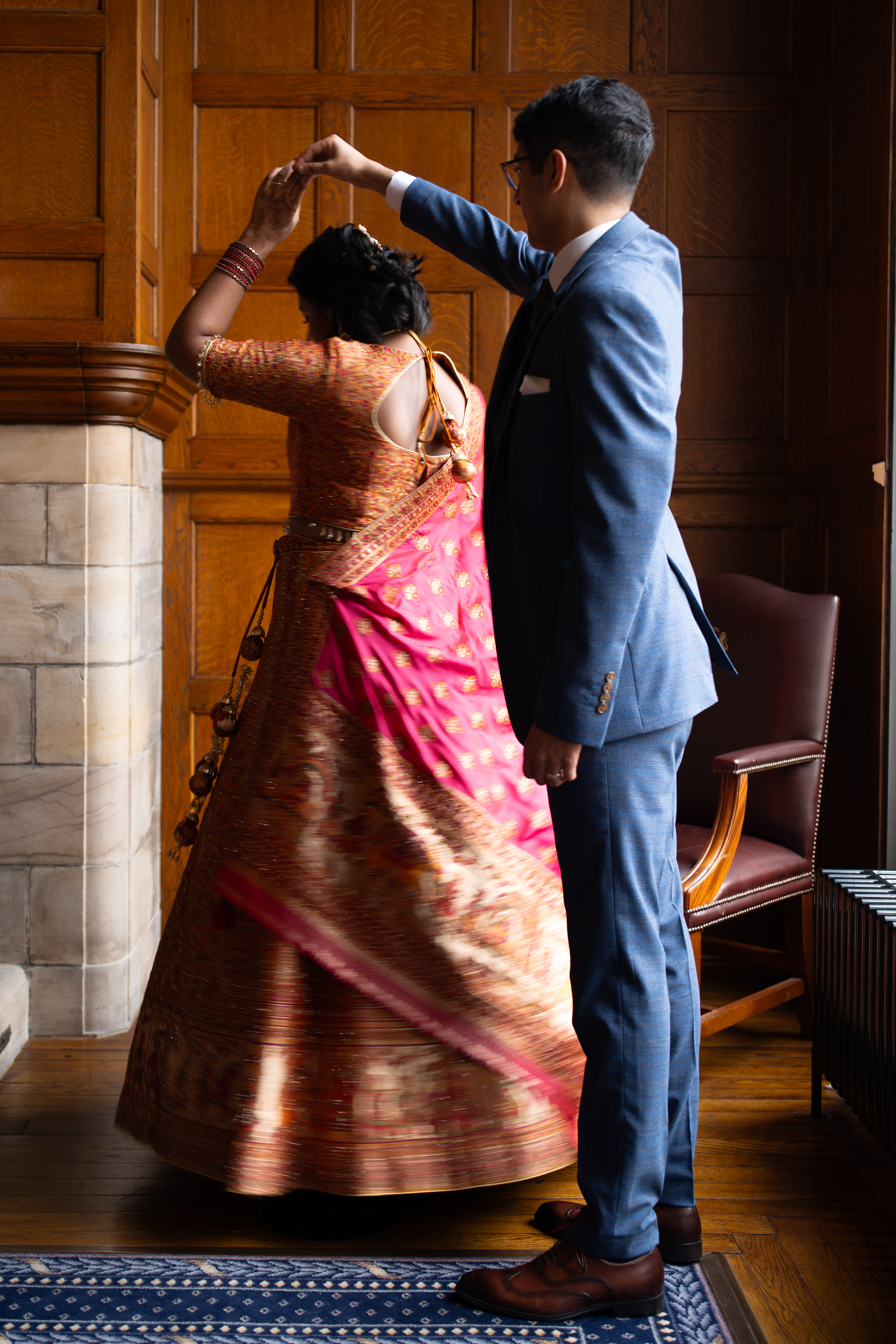 A groom in blue spins bride in orange and pink under his arm in the corner of the Grant Room.