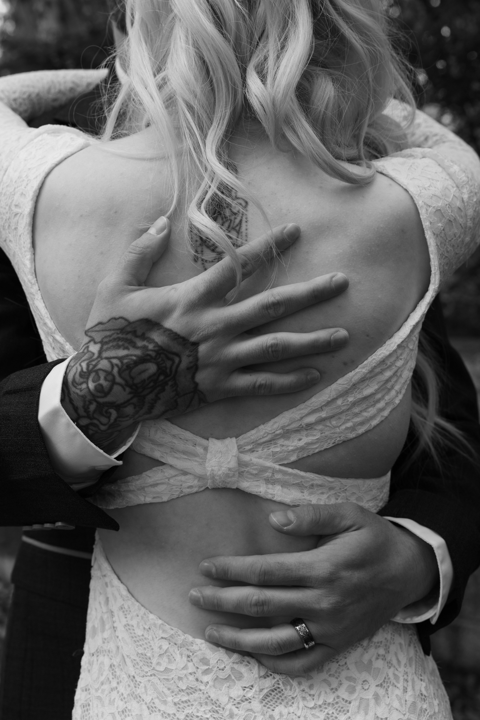 Alternative Aberdeen wedding photographer: Black and white photo of groom's tattooed hands on his new wife's back; she is wearing an open backed dress.