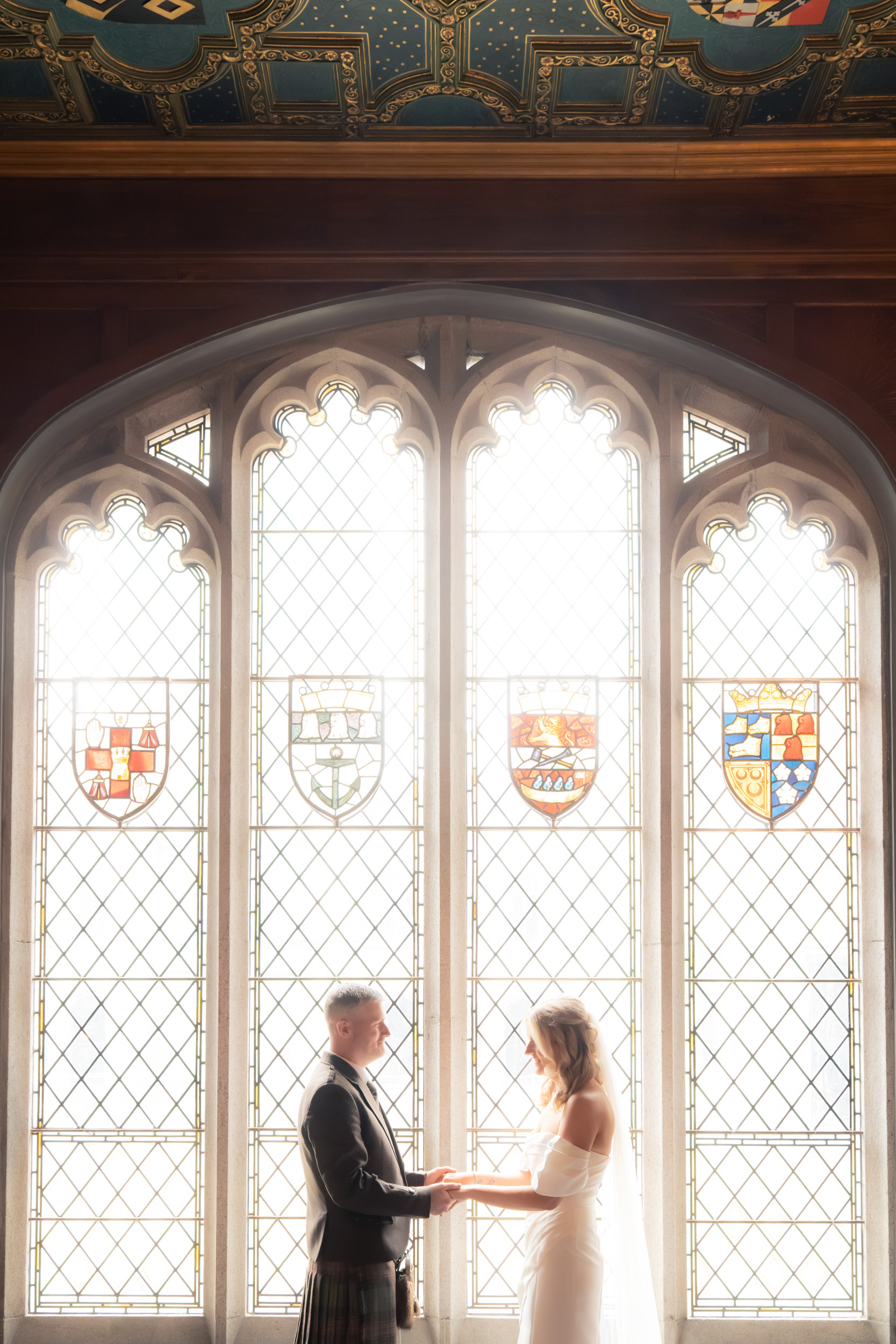 Aberdeen registry office wedding: Bride and groom hold hands in front of glowing stained glass window in Marischal College.