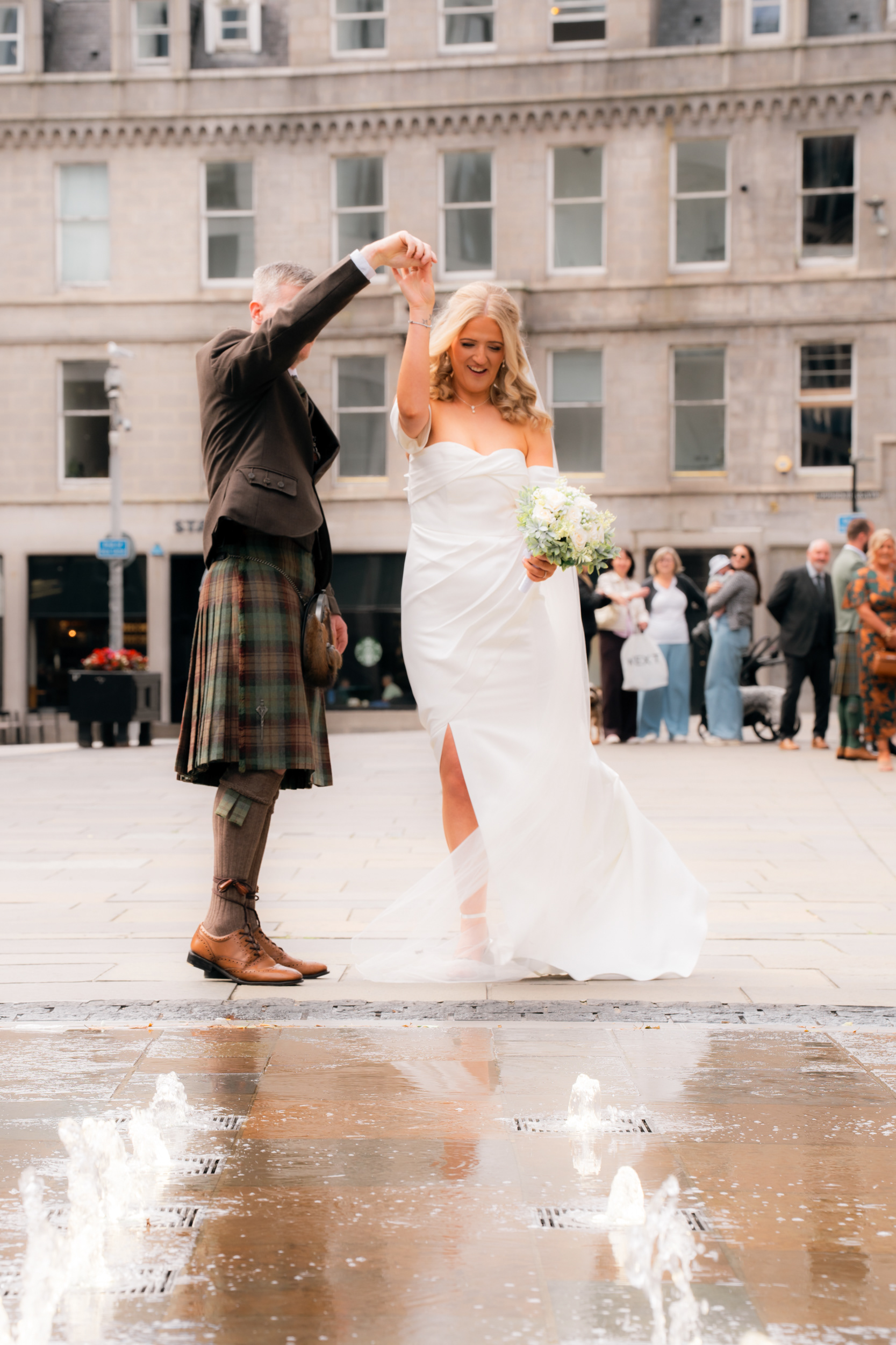 Aberdeen registry office wedding: Bride and groom dance by the Broad Street fountains as guests look on.