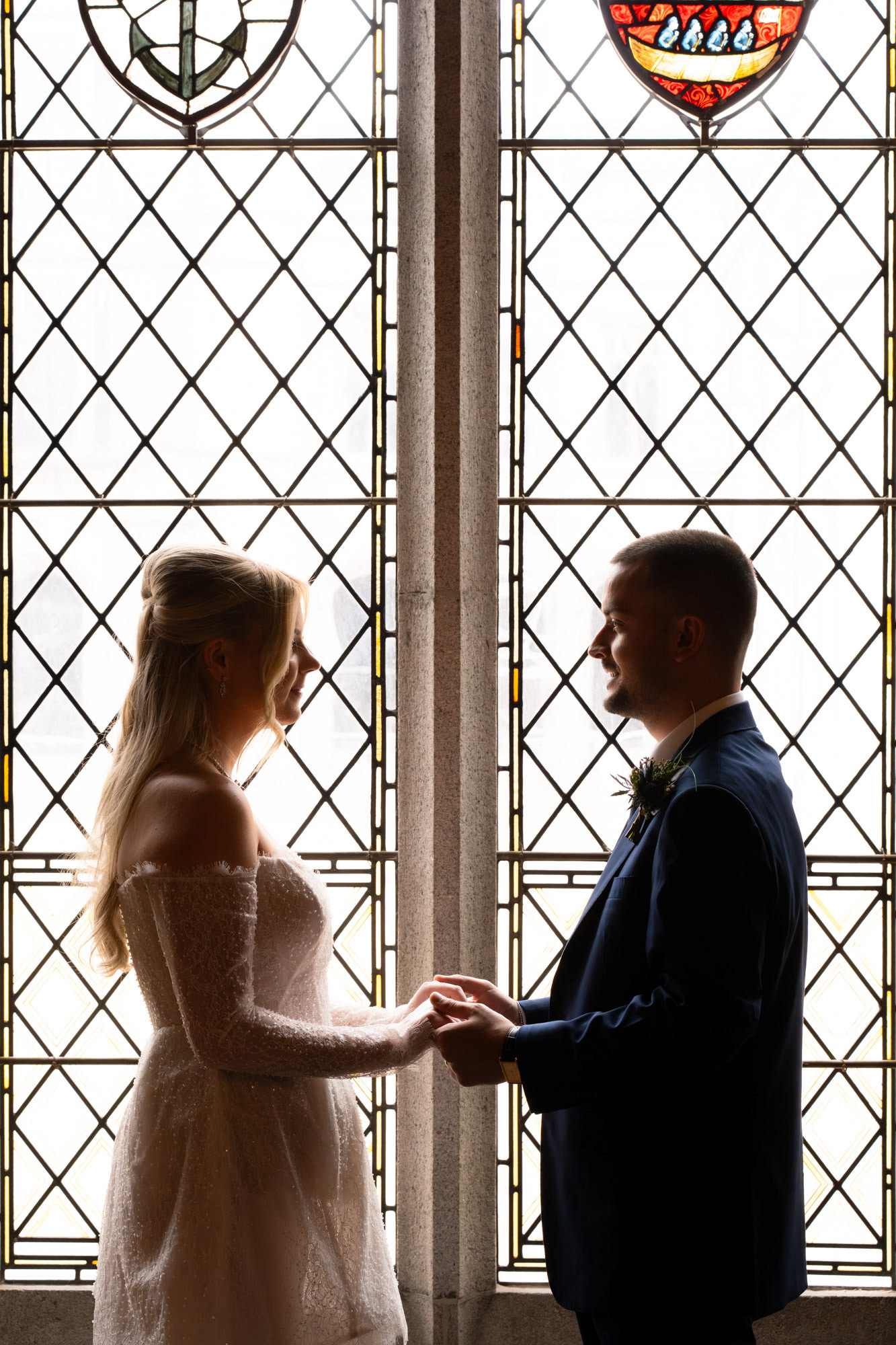 Bride and groom are shown silhouetted against a stained glass window.