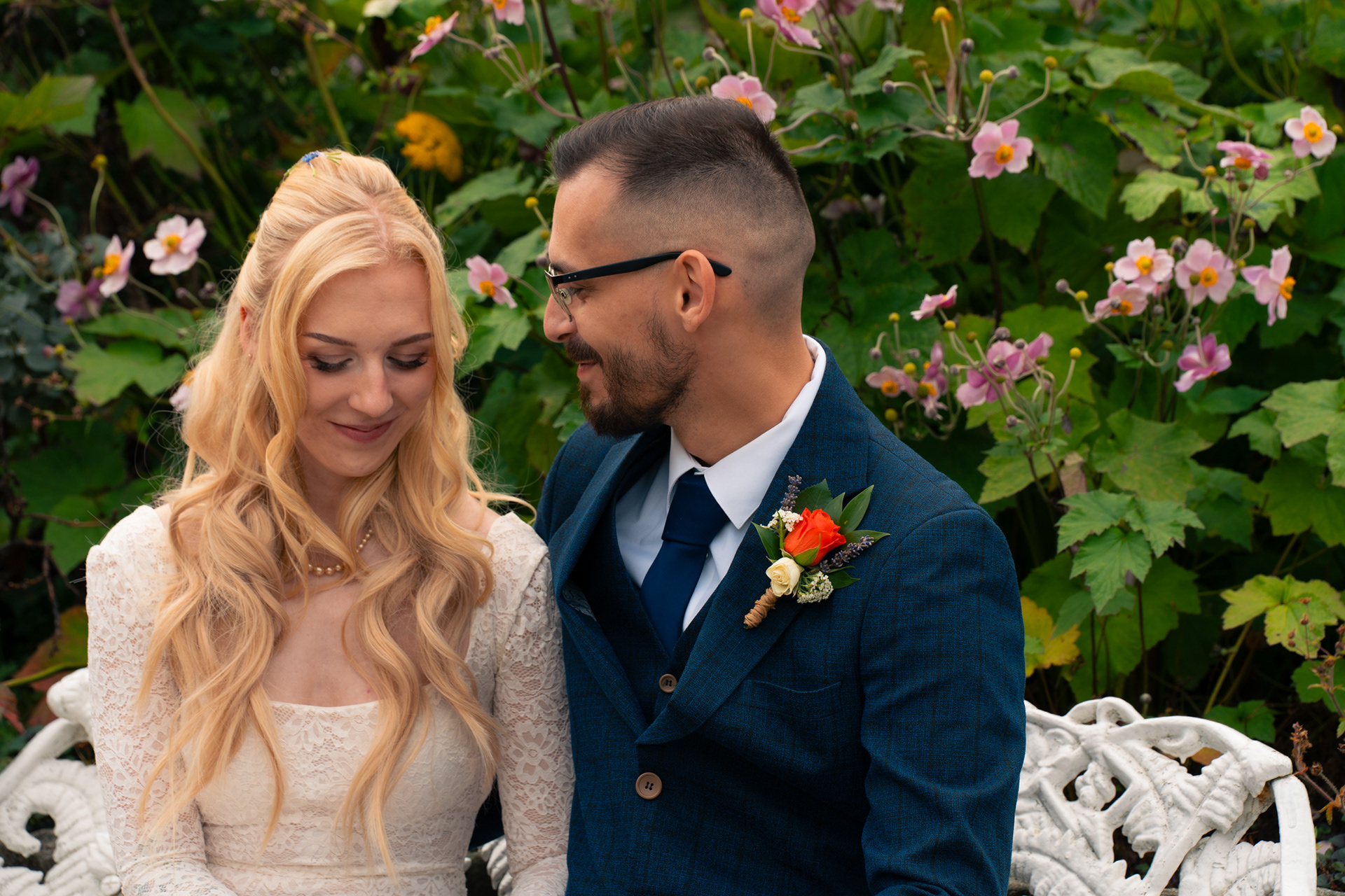 Duthie Park Winter Gardens wedding: Bride and groom sit together on a white bench, surrounded by pink anemones.