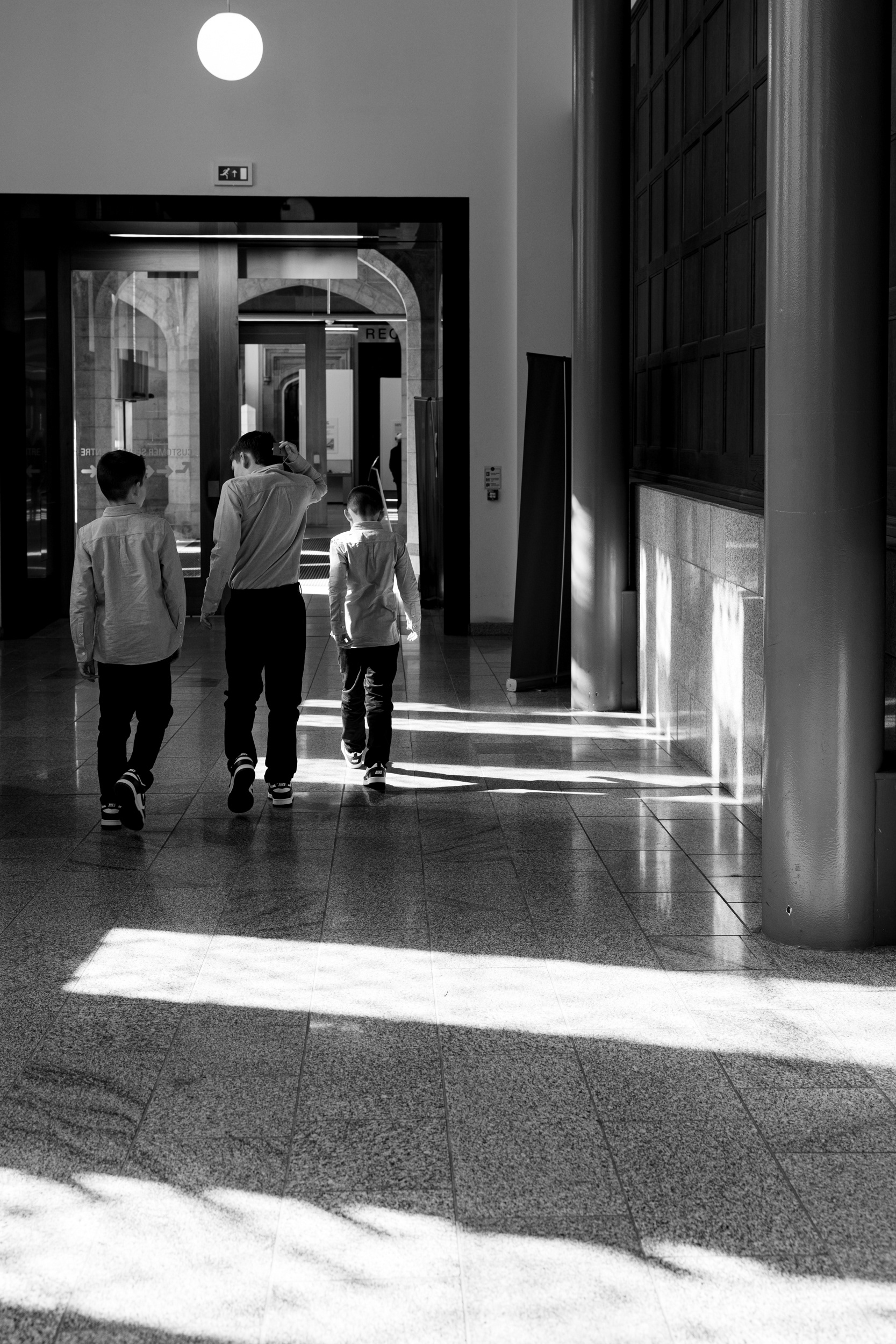 Marischal College wedding: three boys in suits and smart trousers walk away from the camera, through pools of light from stained glass windows.