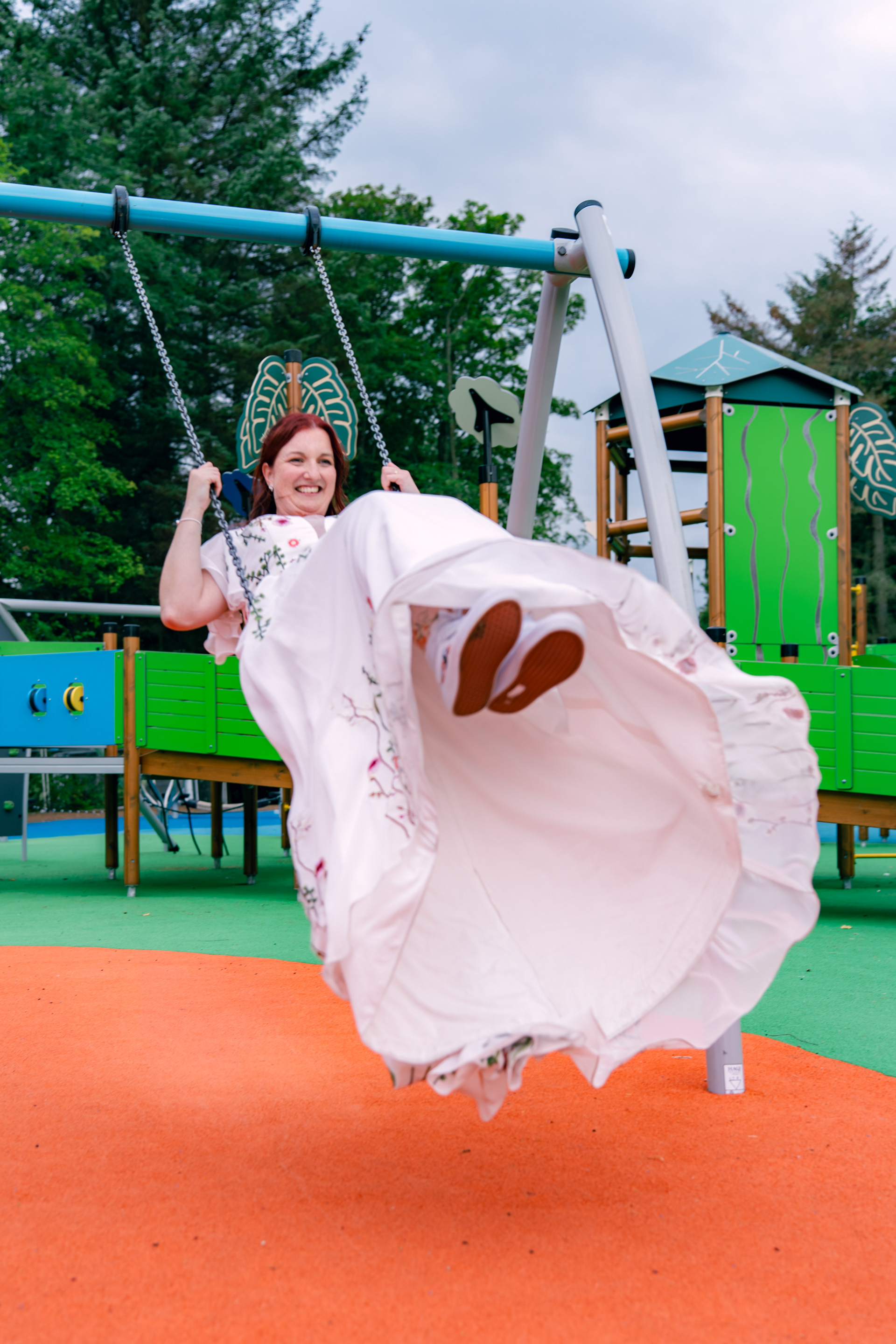 A bride's dress swooshes out as she plays on the swings during her Aberdeen wedding. Her personalised Converse shoes are visible.