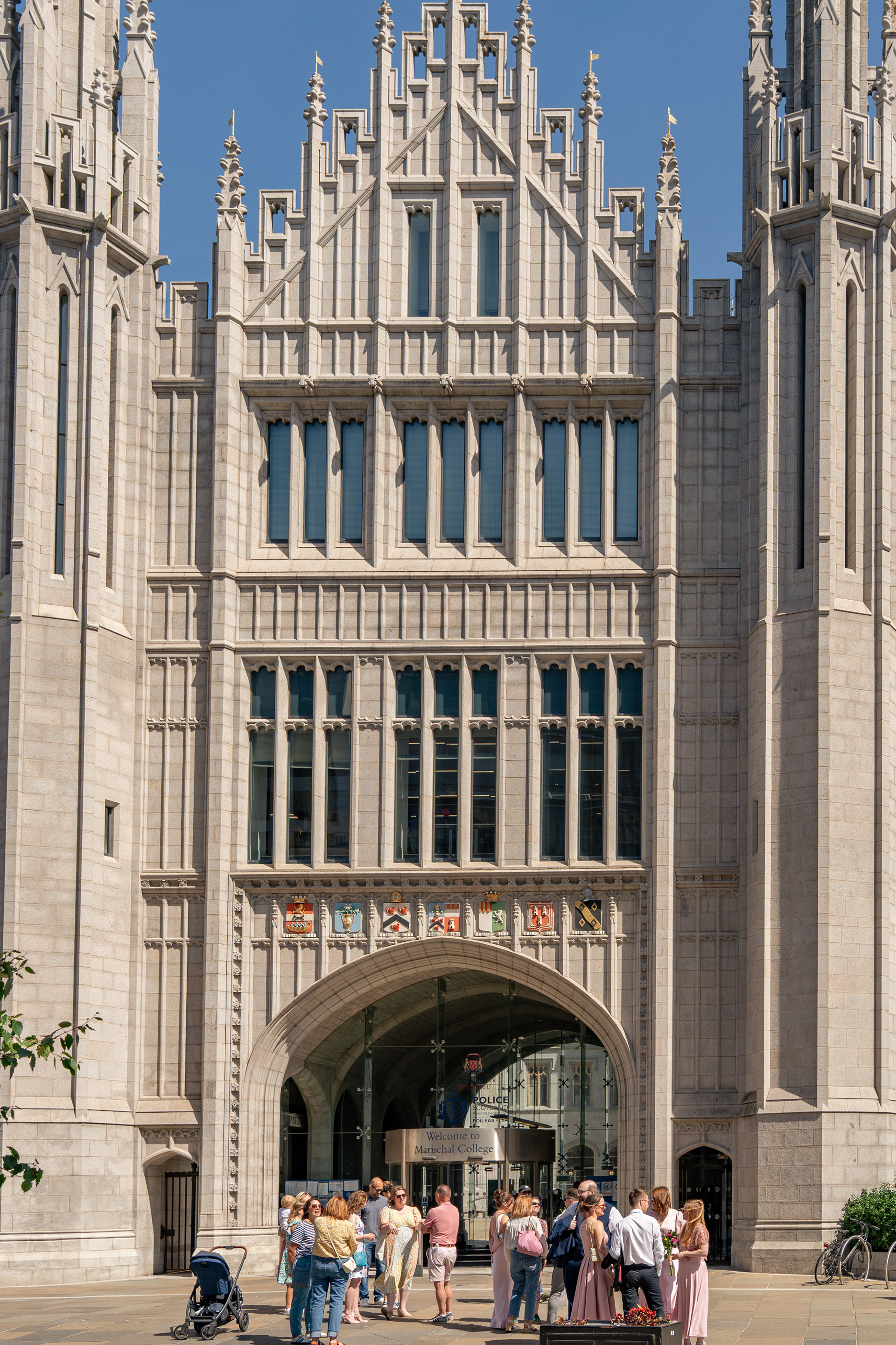 A group of friends and family gather around newlywed bride and groom outside Marischal College in Aberdeen; the full frontage of the building from the door upwards is shown, including tall windows and... um... spiky bits..