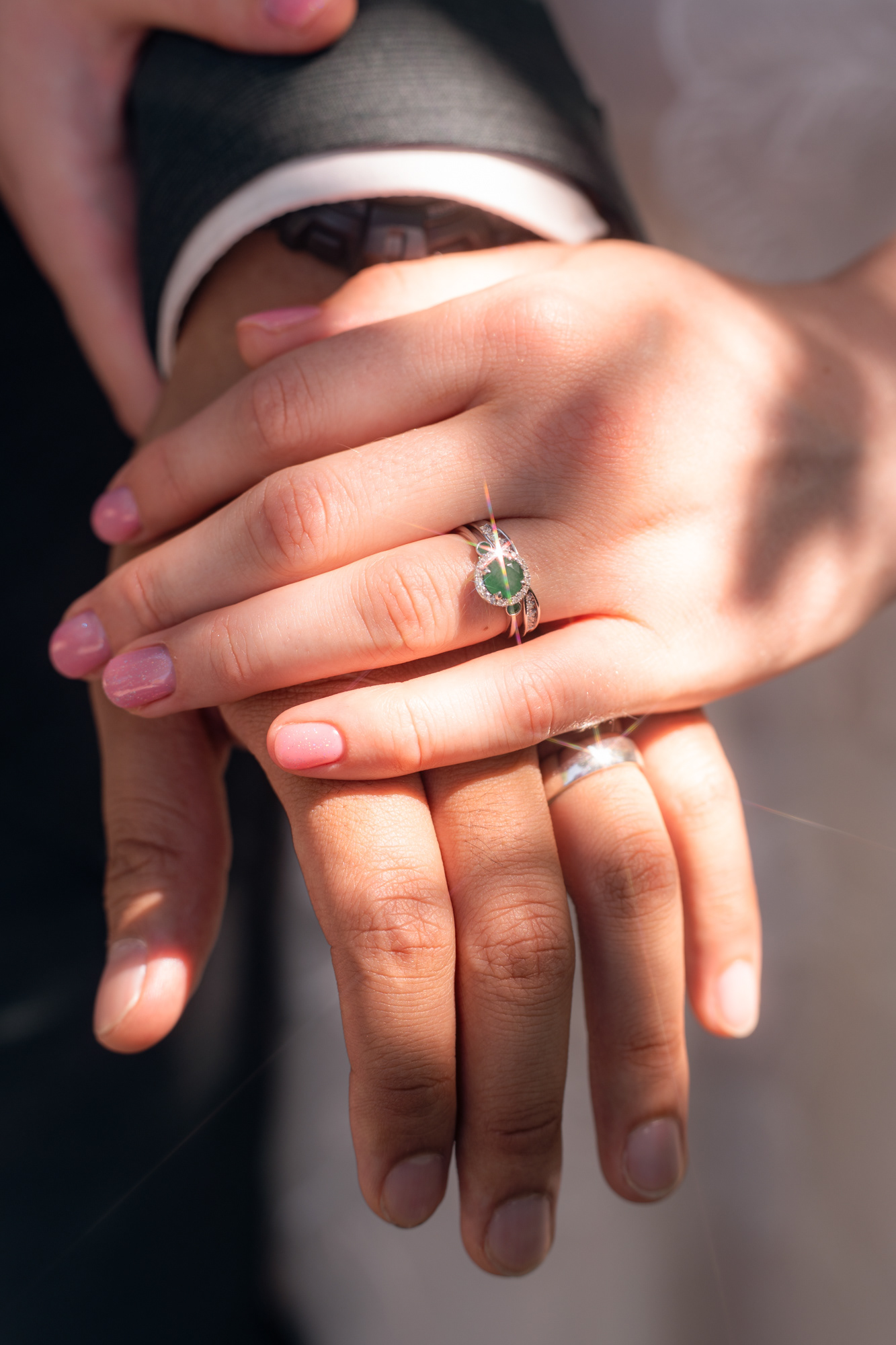 Detail shot of two hands laid one on top of the other, wedding rings visible, bursts of sunlight bouncing off them.