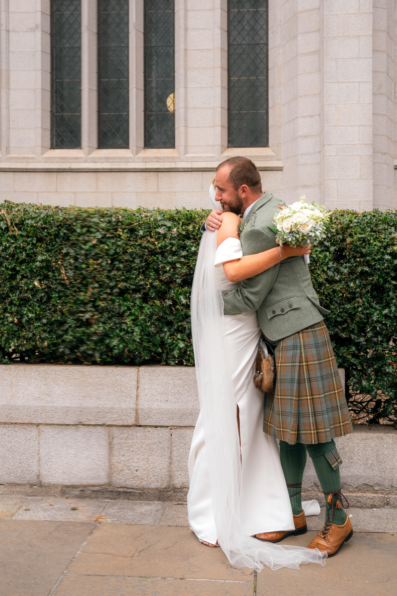 Marischal College wedding: Bride in white hugs her brother in green kilt.
