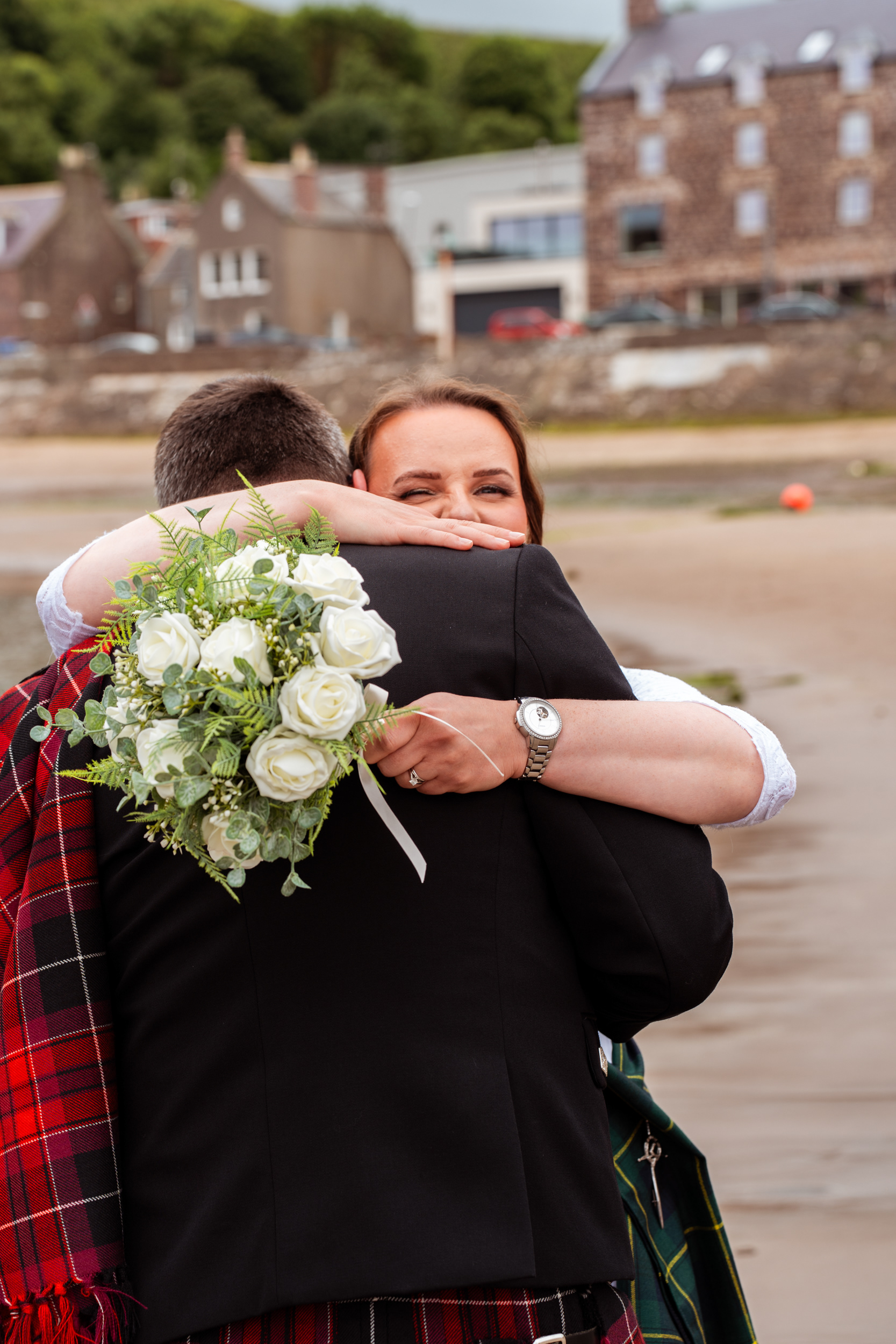 Bride's face is visible as she laughs and hugs her new husband during their Scottish elopement at Stonehaven.