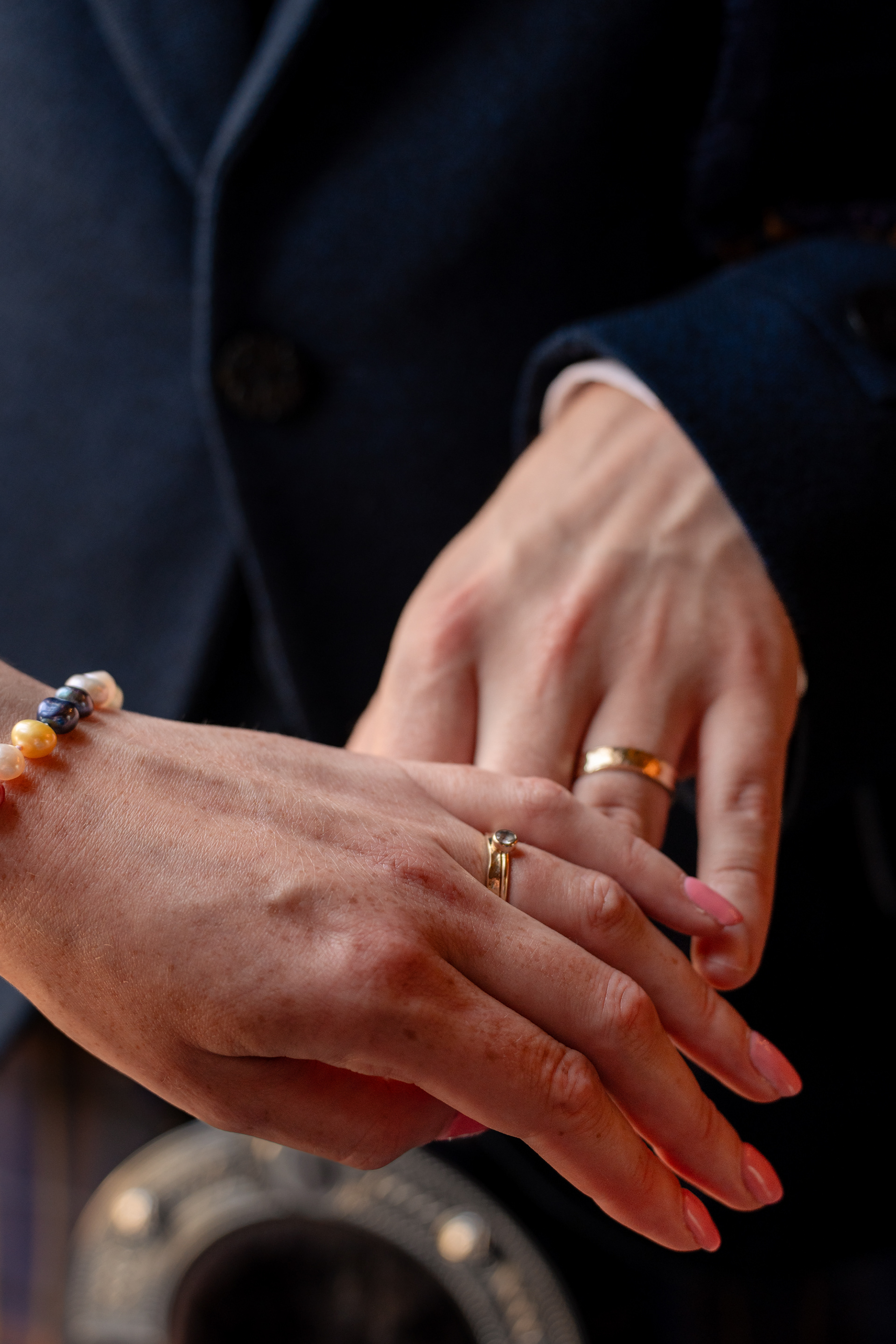Close up of bride and groom's hands (both white skinned) with gold wedding rings visible.