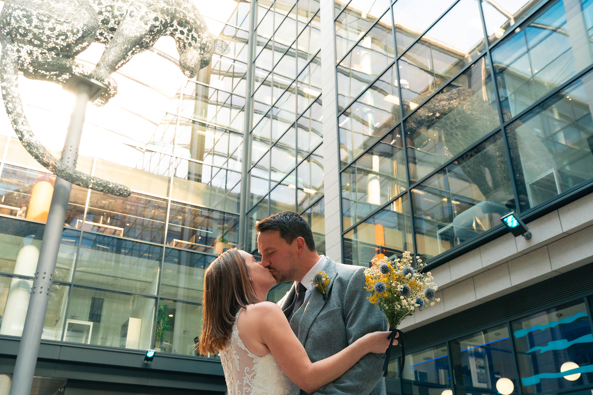 Bride and groom kiss under cat statue after their Marischal College wedding in Aberdeen. The bouquet and the background are full of blues and yellows.