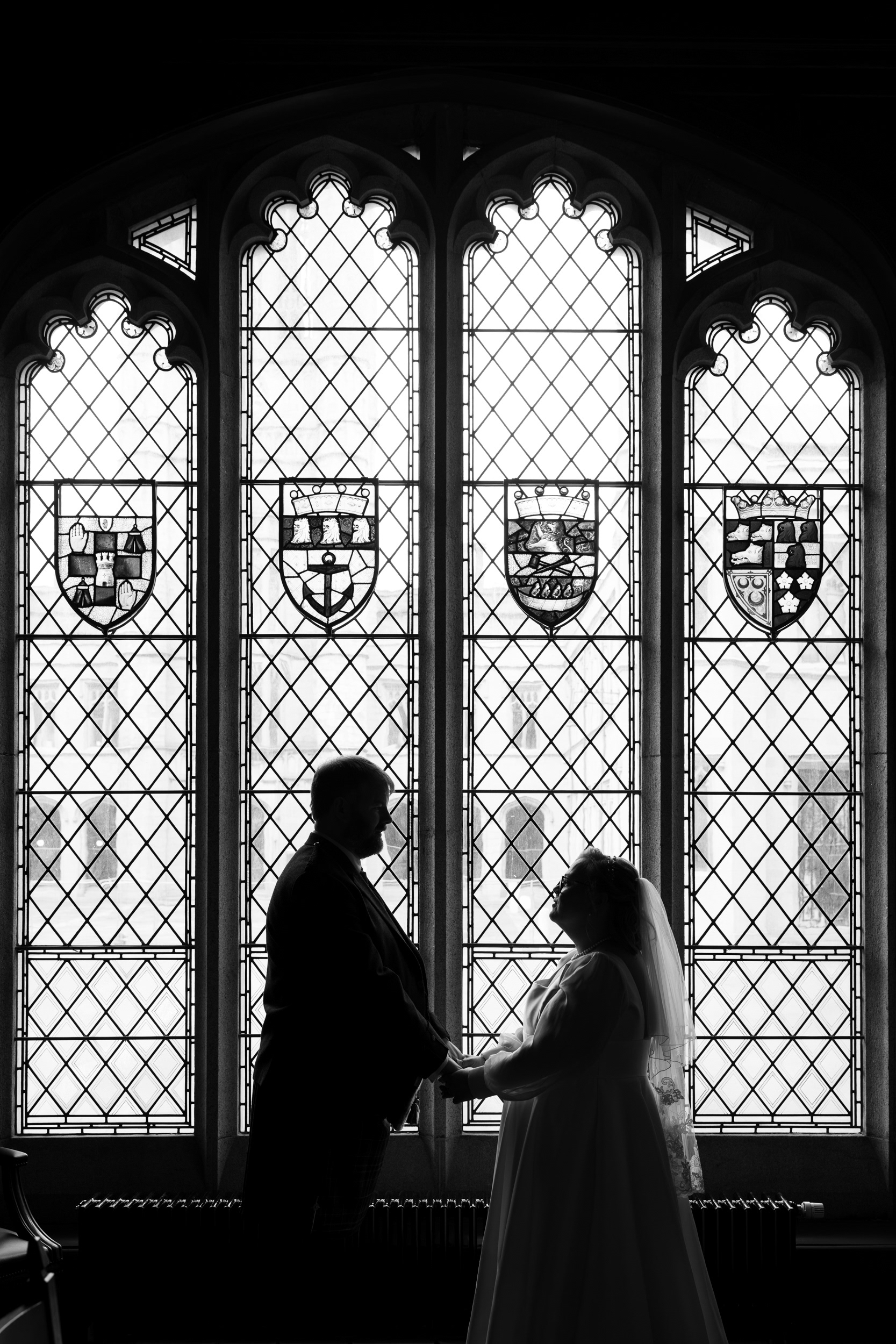 Aberdeen wedding photographer: Marischal College registry office wedding. Black and white photo of couple silhouetted against stained glass window.