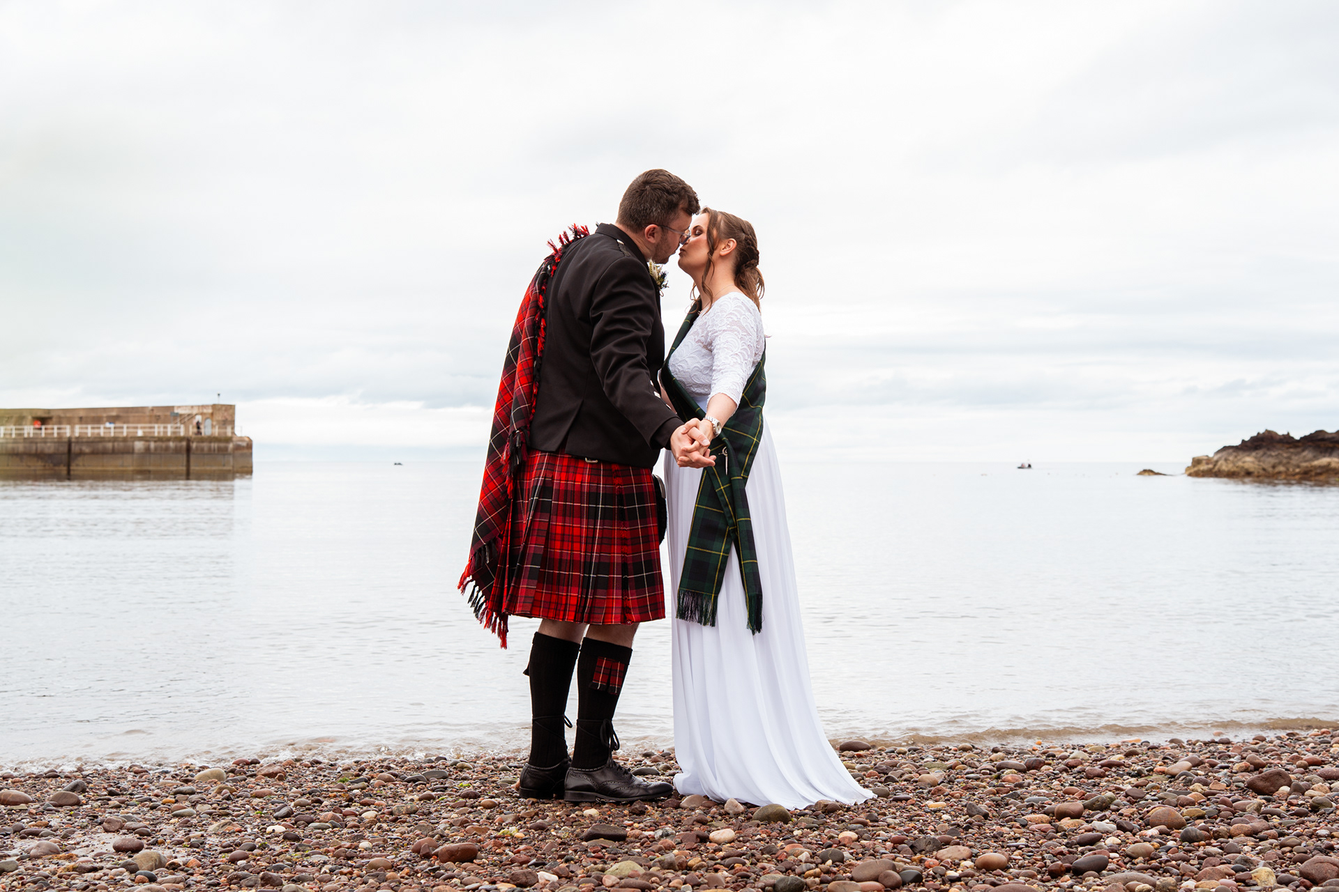 Secret Stonehaven registry office wedding - bride in white with tartan sash and groom in red kilt kiss against a backdrop of Stonehaven harbour, near Aberdeen.