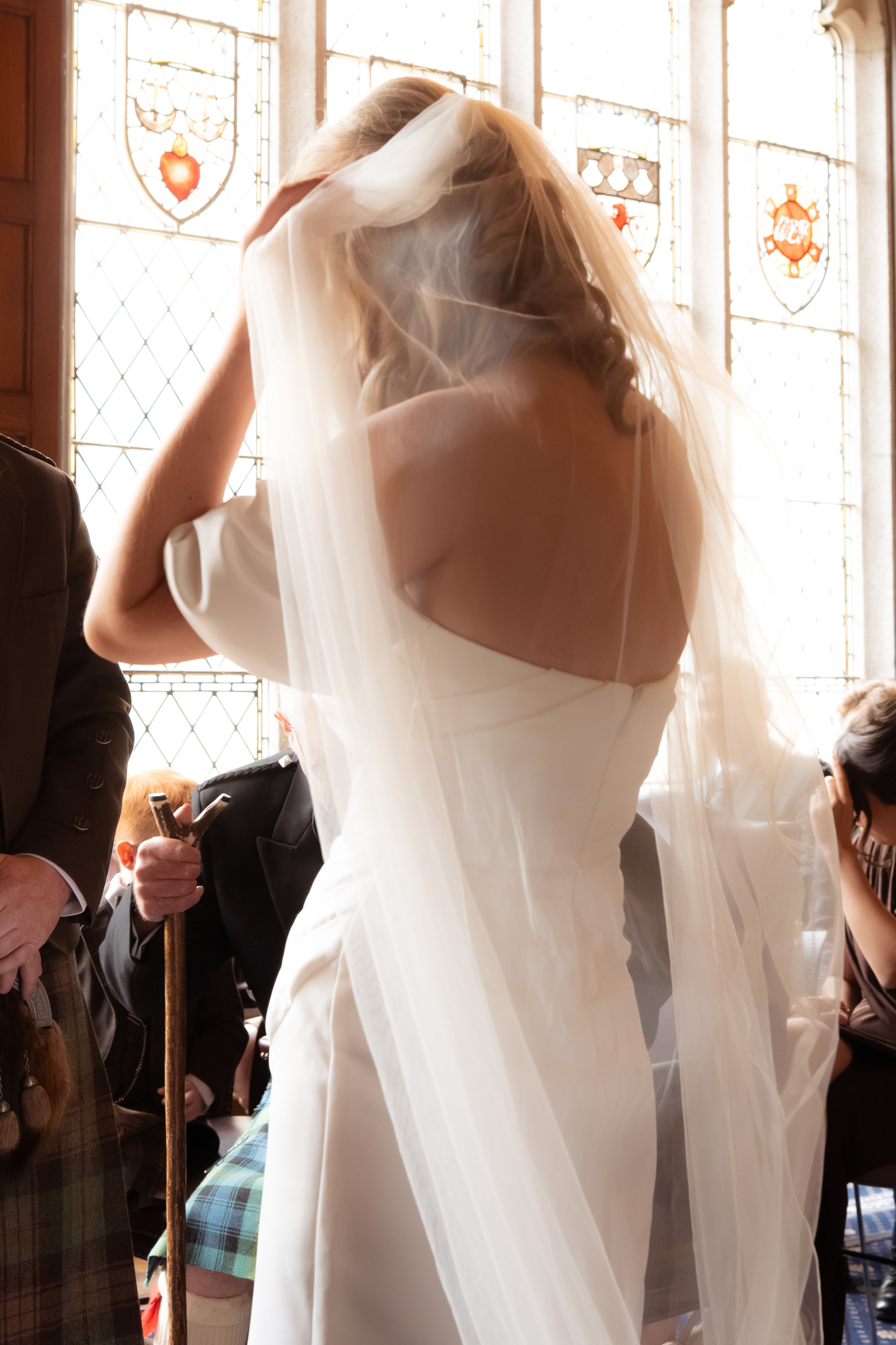 Aberdeen registry office wedding: A bride adjusts her veil, backlit by the stained glass windows in Marischal College.