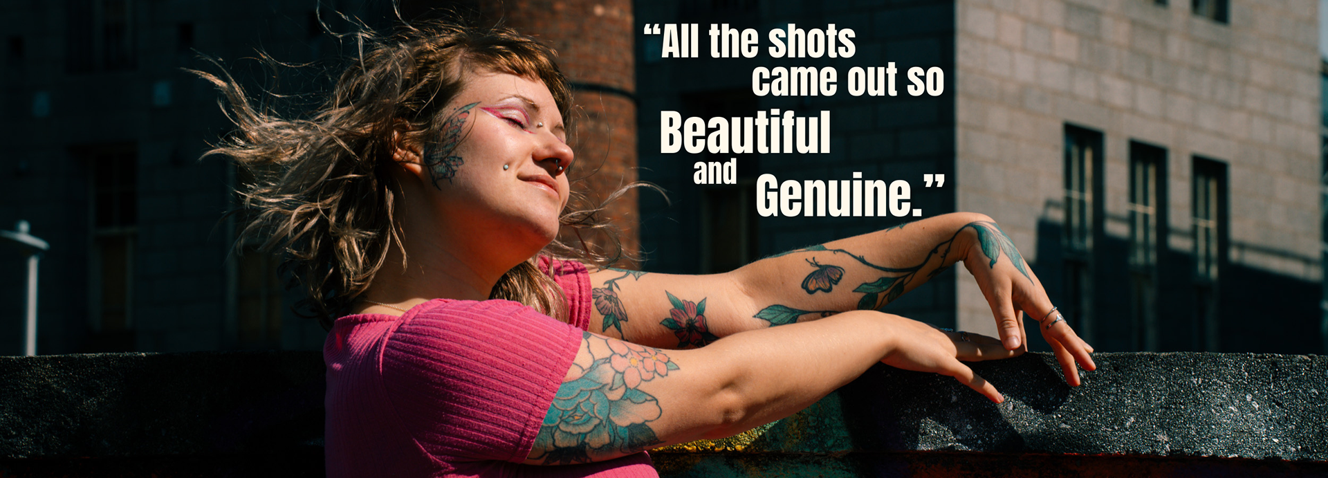 Young woman in pink with tattoos, piercings and short hair blowing in the wind. Review text reads:"All the shots came out so beautiful and genuine."