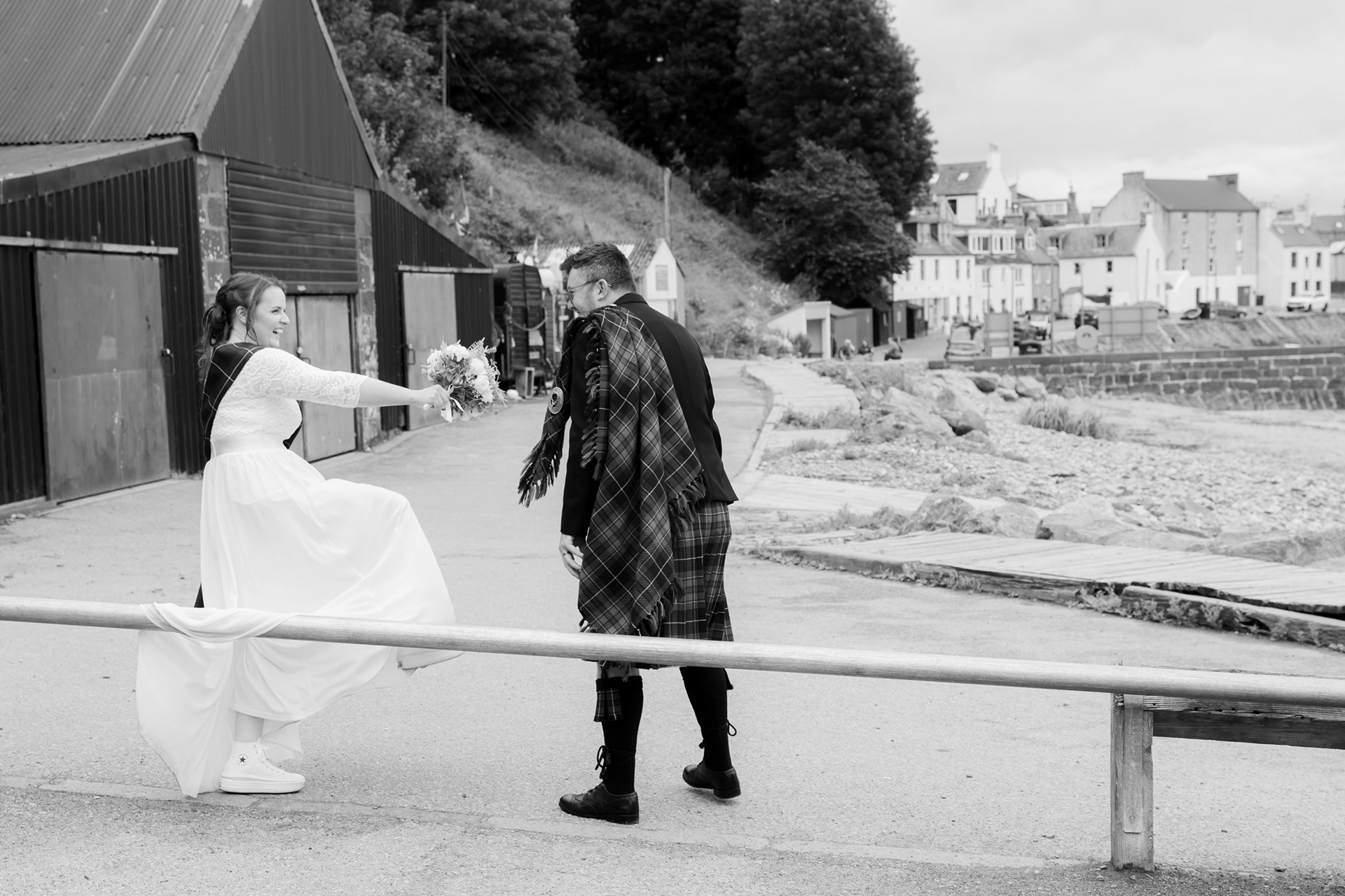 Relaxed Aberdeenshire wedding photography: Bride and groom laughing as bride climbs over a low barrier in her big white wedding dress - good things she's wearing Converse!