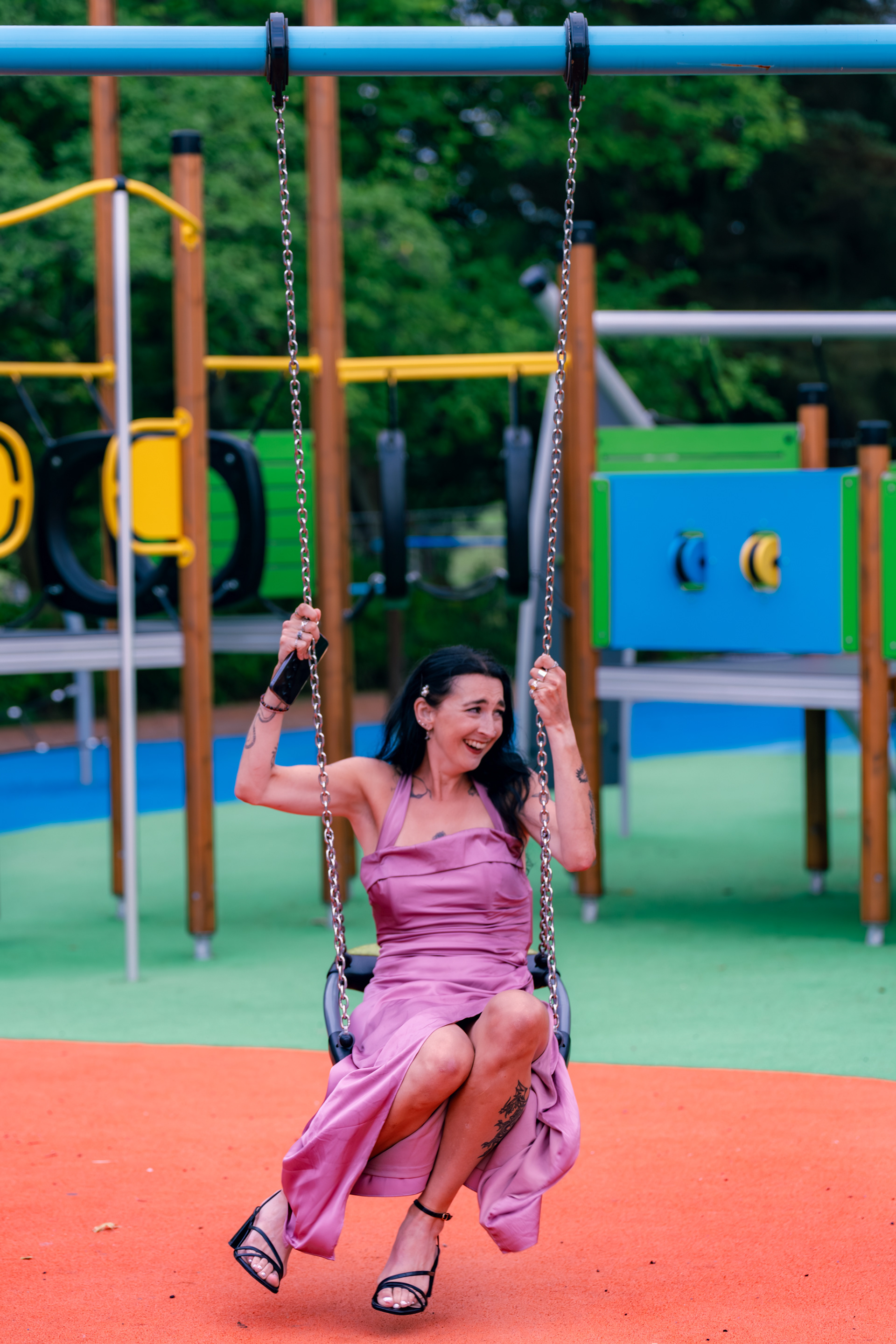 A young woman in a dusky pink bridesmaid dress laughs on the swings at Hazlehead during an alternative Aberdeen wedding