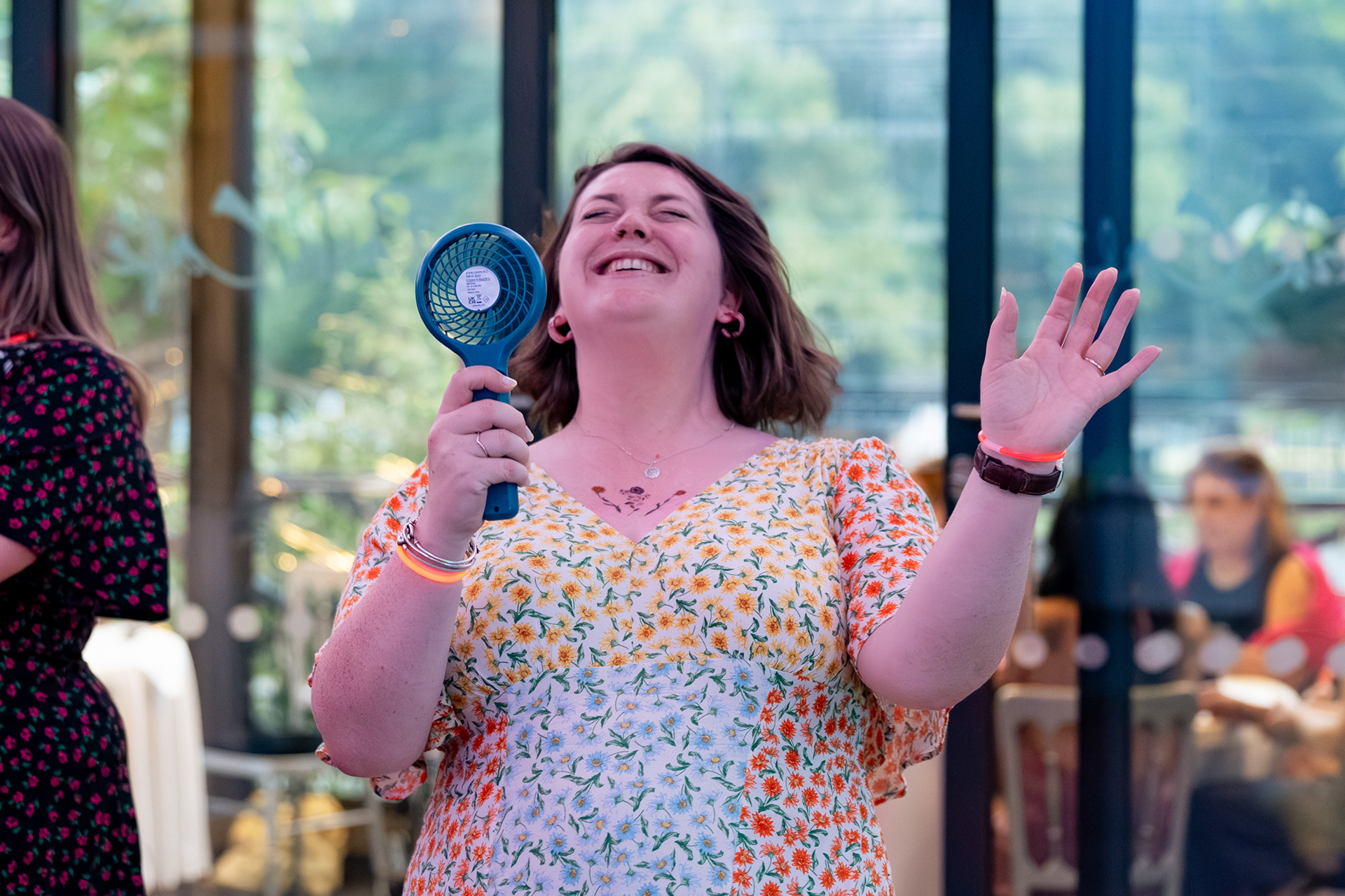 A woman in a floral dress laughs as she holds a fan up her face while she dances at an Aberdeen wedding