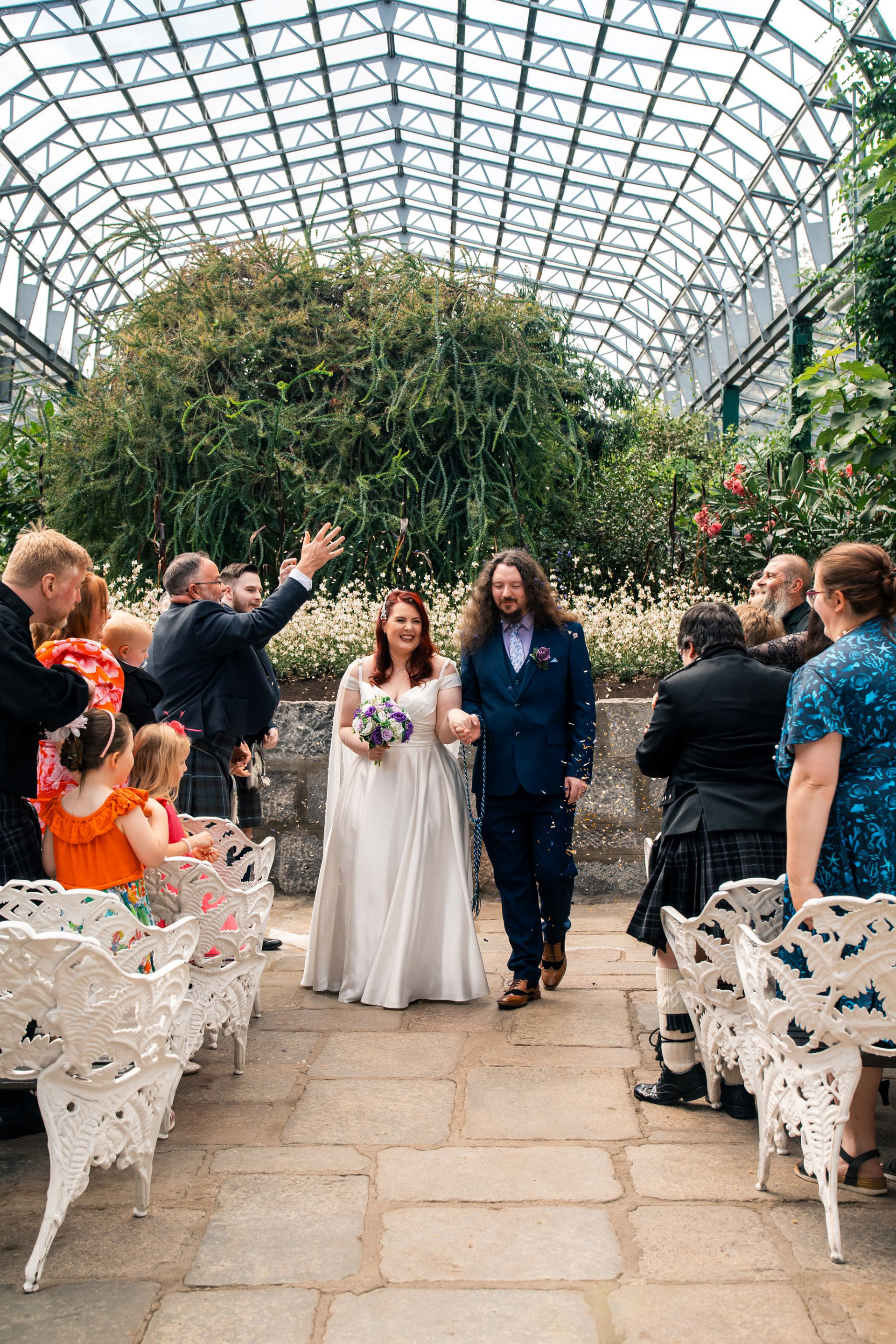 A bride and groom walk hand in hand back down the aisle at Duthie Park as their guests cheer.