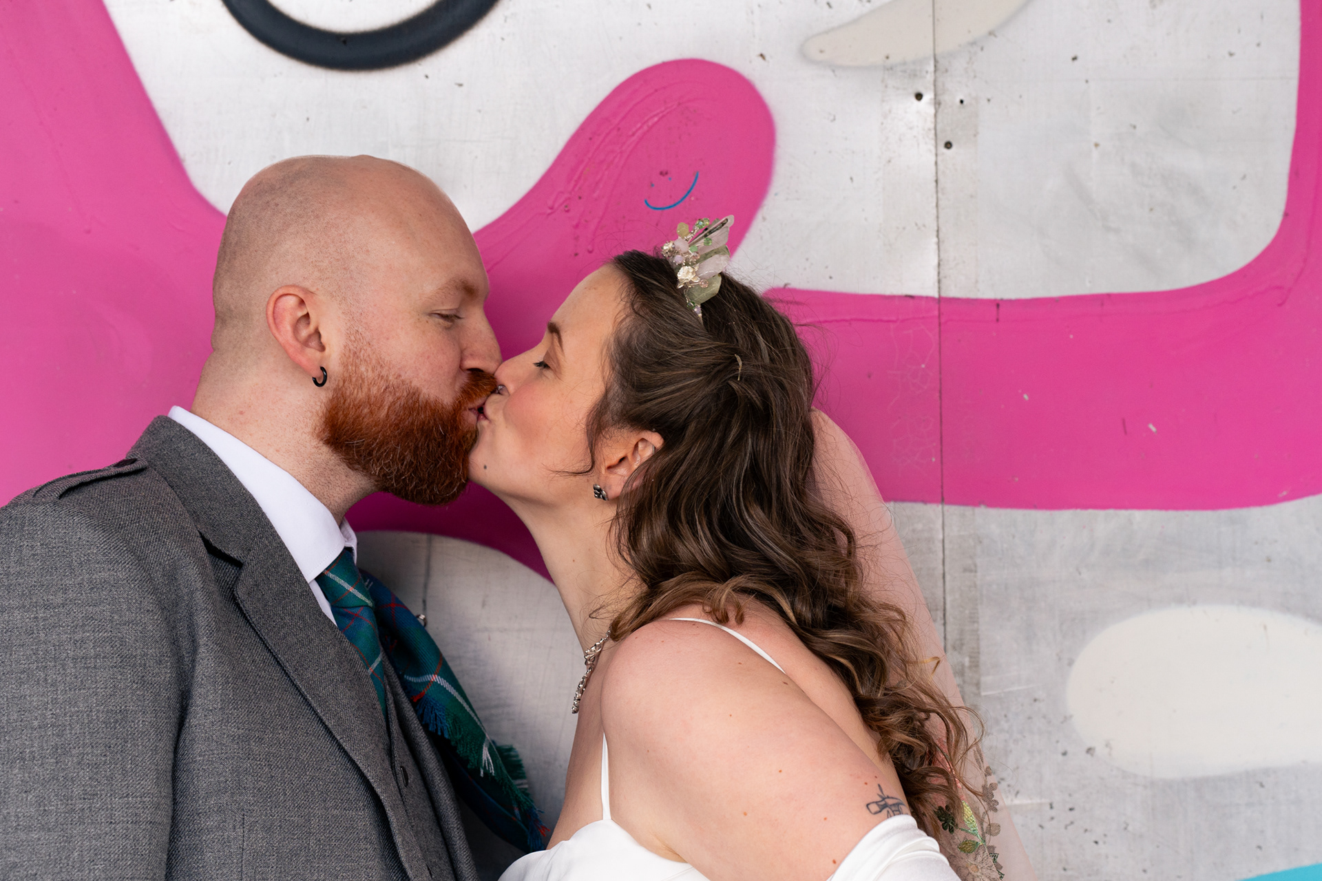 Alternative Aberdeen Wedding Photography: Bride and groom kiss underneath a tiny graffiti smiley face.