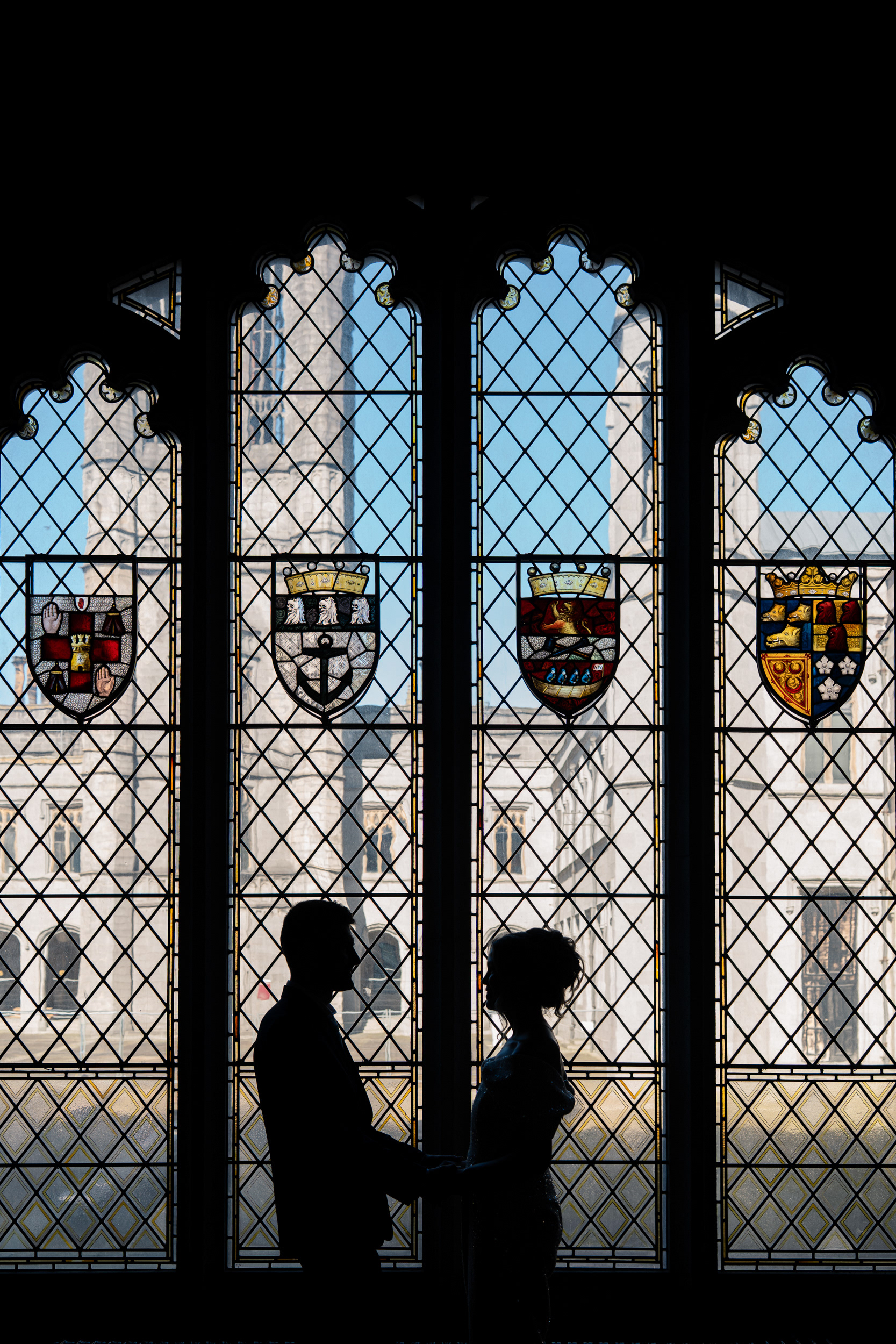 Bride and groom are silhouetted against the stained glass windows in Marischal College's Grant Room after their Aberdeen micro-wedding.