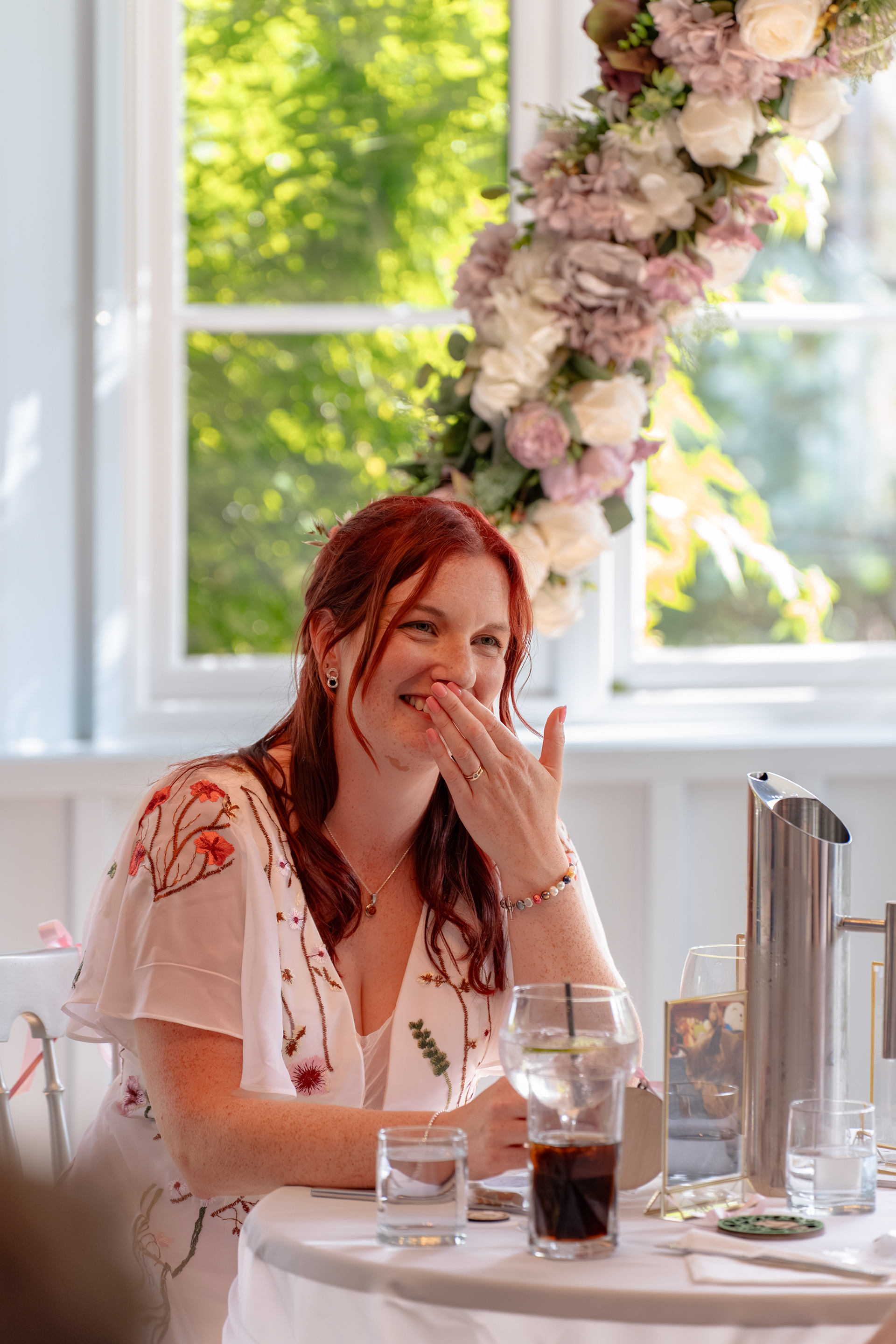 A bride covers her mouth and laughs during her sister's speech