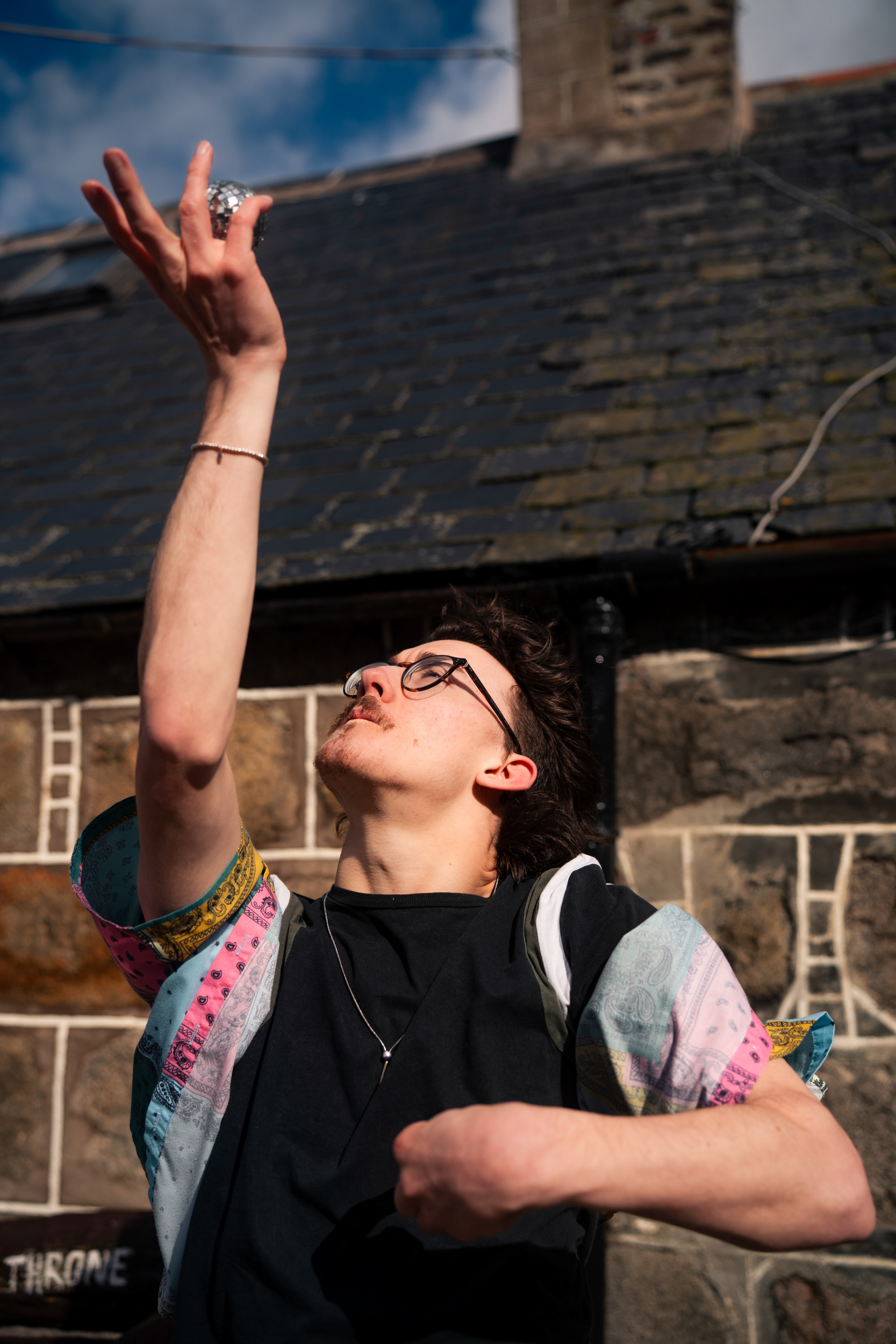 A Disabled man holds a tiny disco ball up to the sky with one hand.