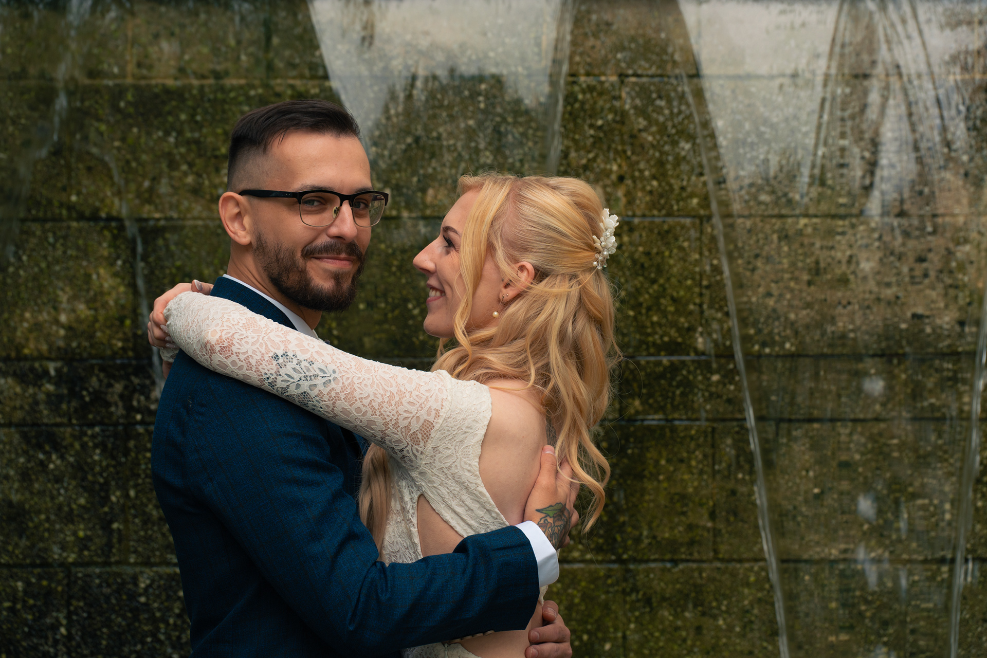 Duthie Park Winter Gardens wedding: Bride and groom embrace in front of a waterfall. She is grinning at him, and he is smiling proudly at the camera.