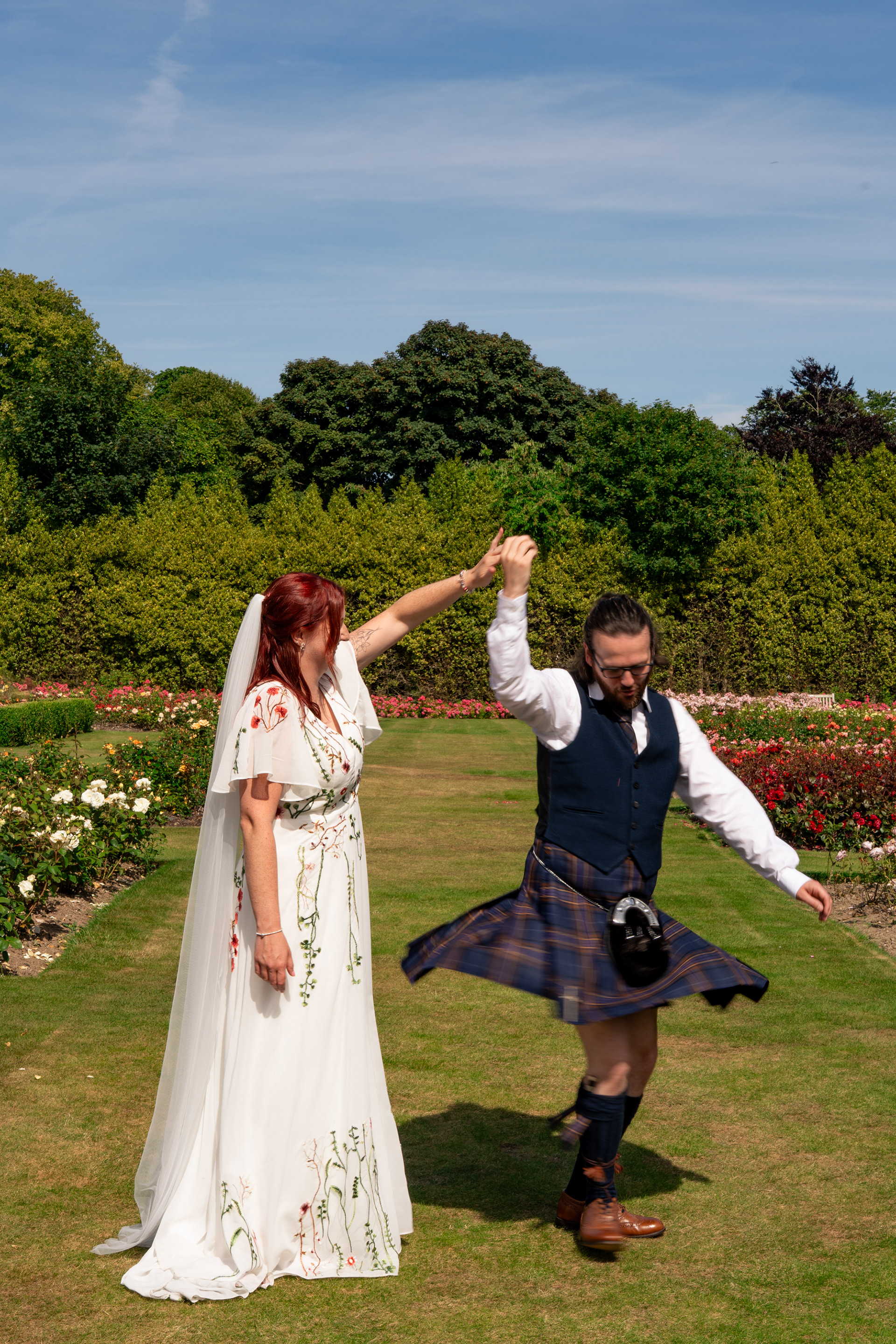 A groom twirls under his bride's arm, his kilt a blur of movement