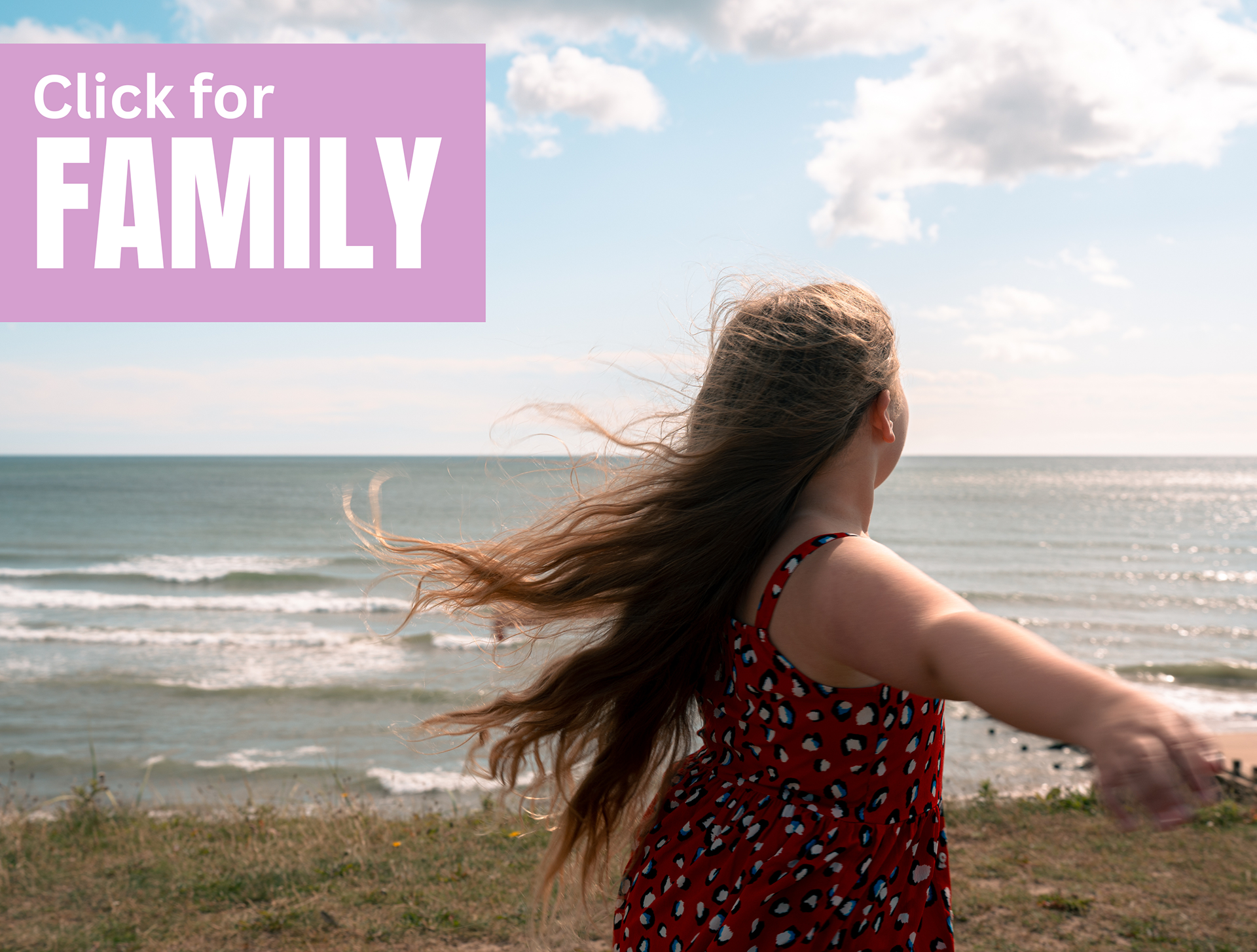 A young girl in a red sundress twirls, her long hair caught by the wind, blowing around her. The backdrop is of the Aberdeen Beach and the sparkling North Sea.