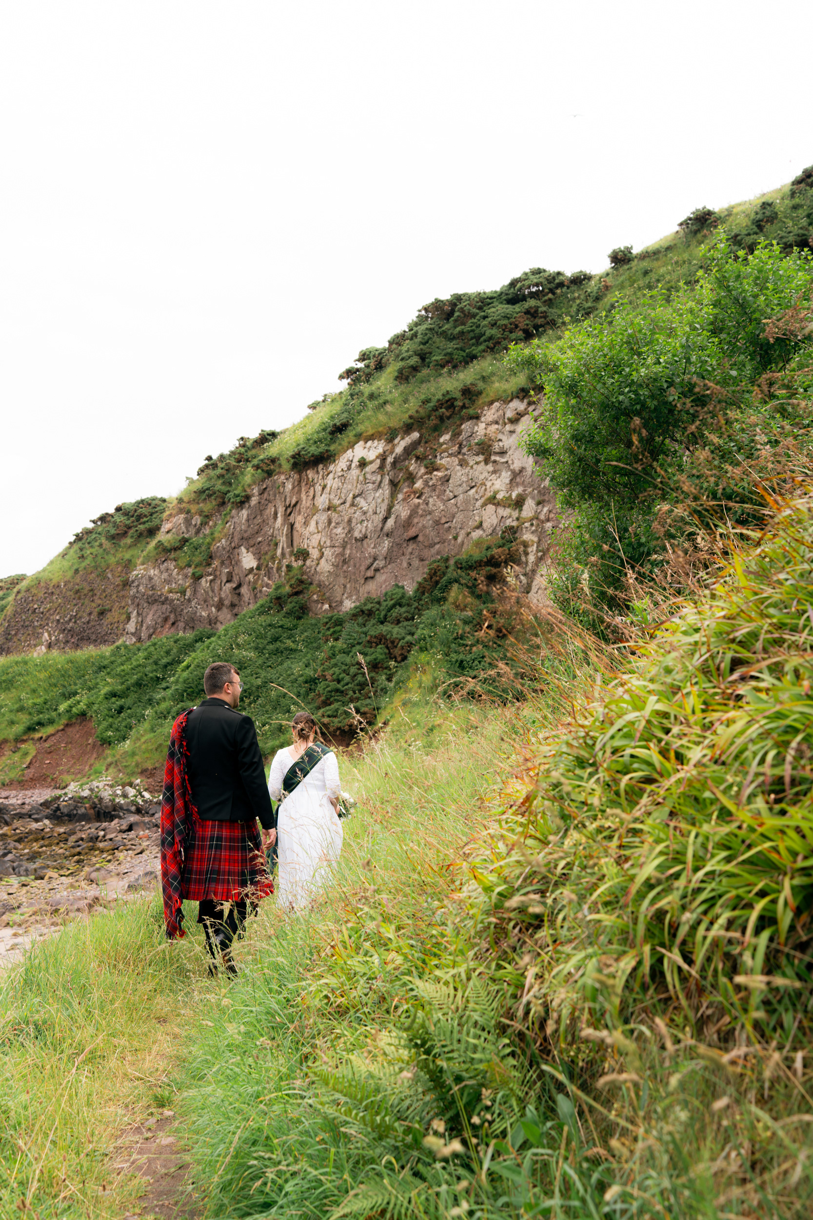 Stonehaven wedding photography: Bride and groom walk through the overgrowth by the sea.