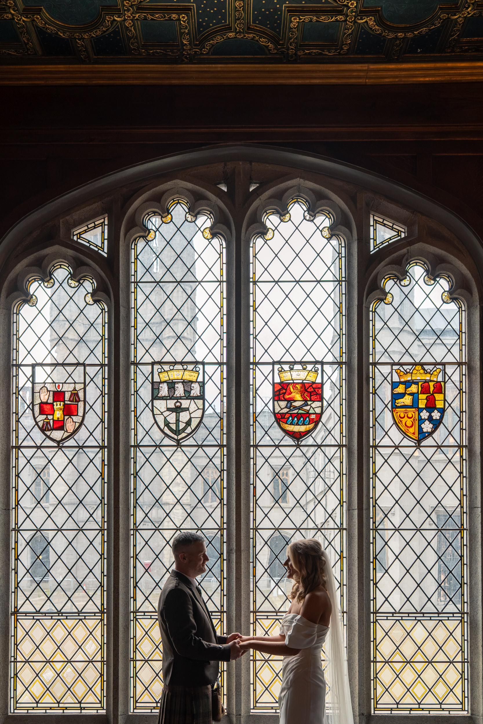 Bride and groom are silhouetted against the stained glass window in Marischal College's Grant Room during their registry office wedding.