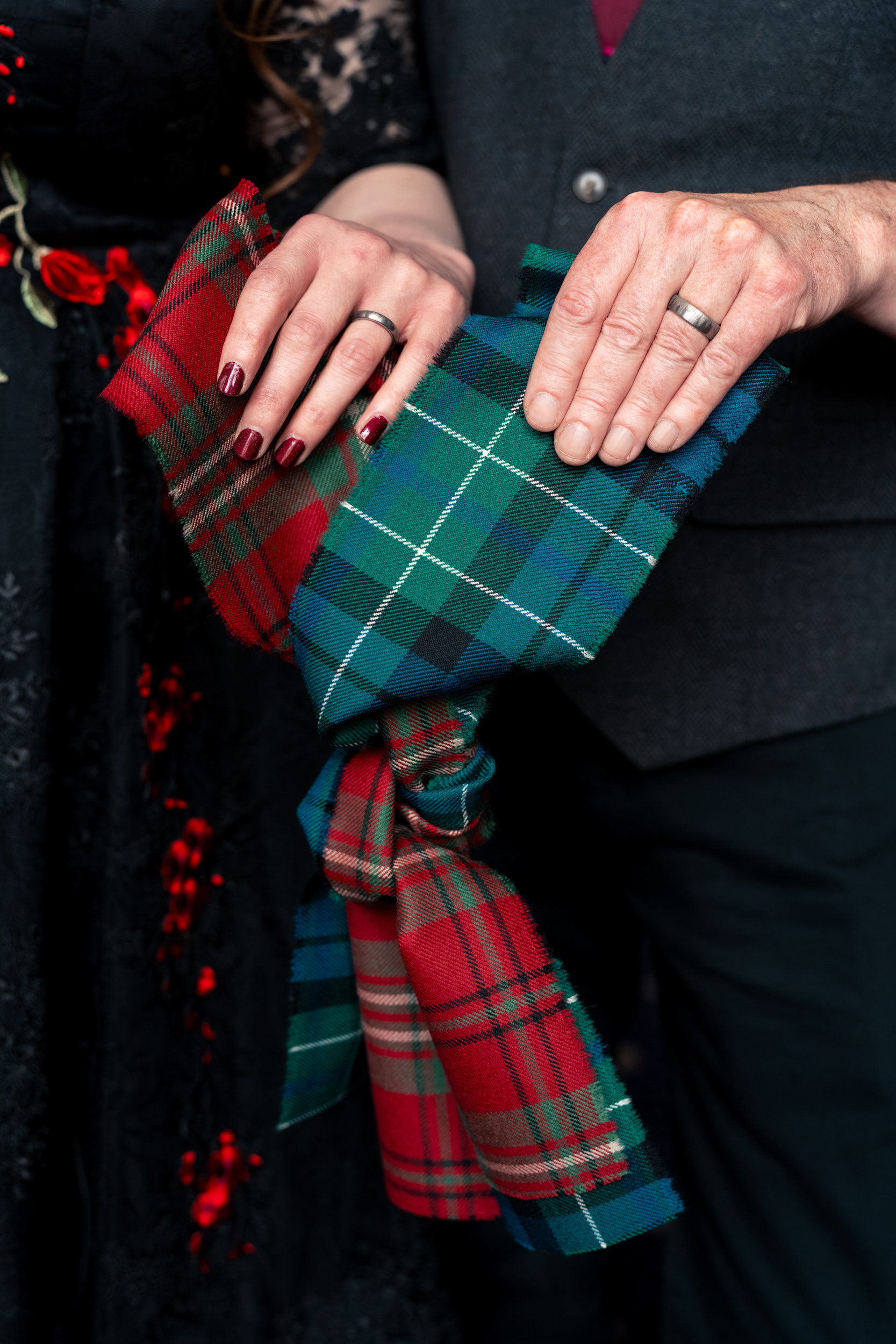 Couple's hands, each with a new wedding ring on their finger, hold the tartan knot they tied during their Aberdeen registry office wedding.