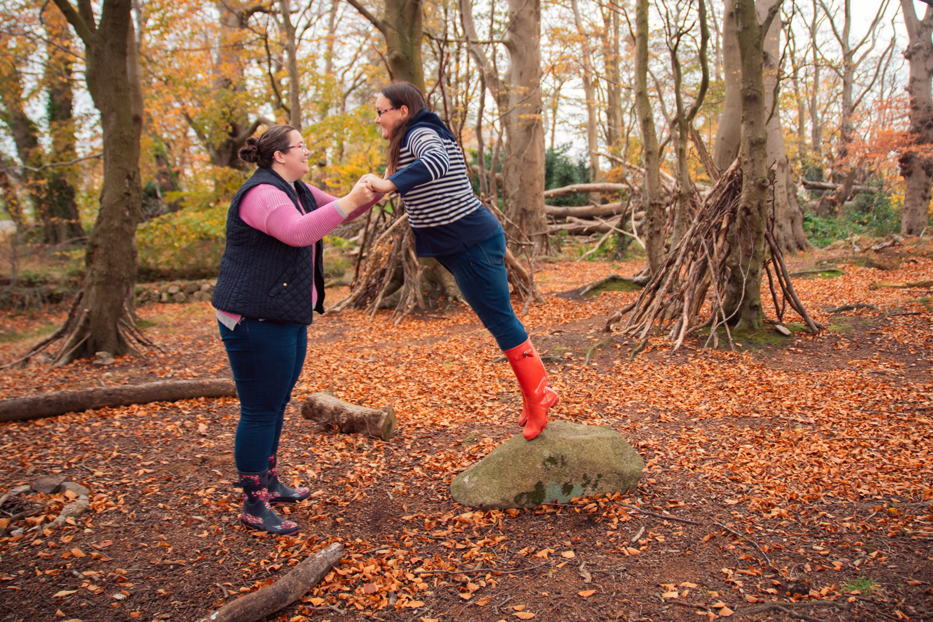 Fun and laughter on an Aberdeen engagement shoot as two brides-to-be hold hands and one leaps off a big rock and into her girlfriend's arms.