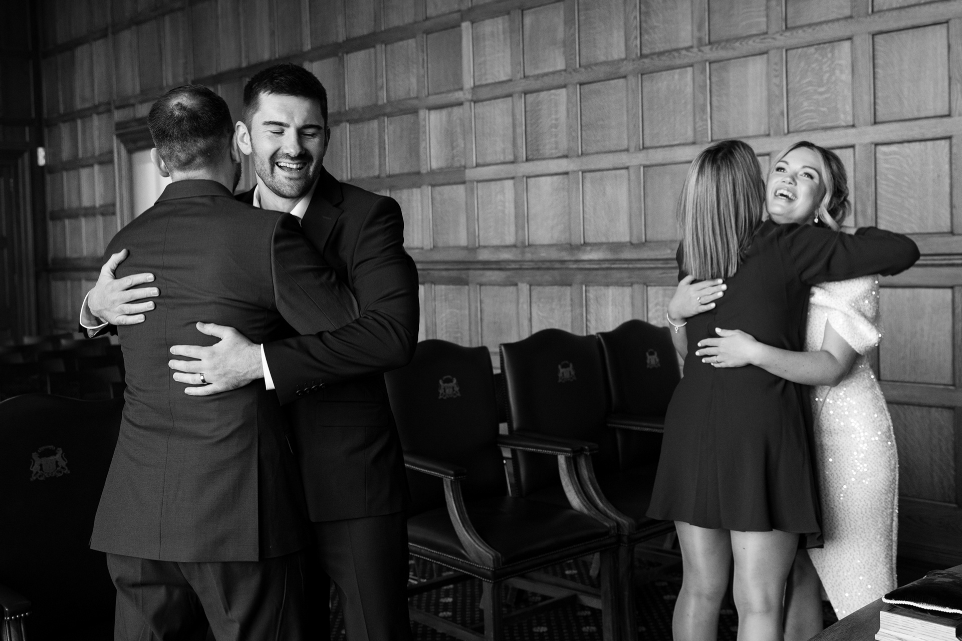 Aberdeen wedding photographer, Sarah from Windswept Stories, took this black and white photo of bride and groom hugging their witnesses, everyone grinning.