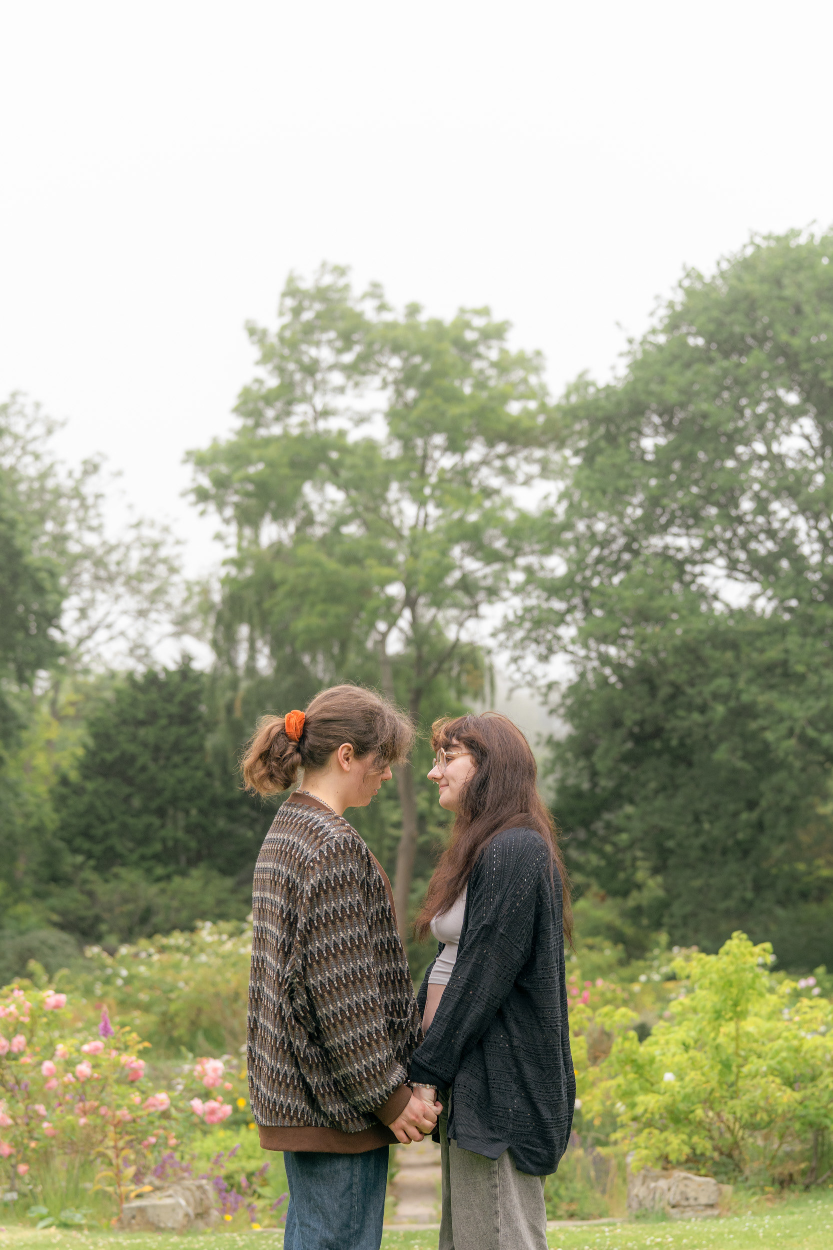 Taken by LGBTQ+ Aberdeen wedding photographer, Sarah from Windswept Stories, two wives hold hands and stand face to face, eye to eye, against a backdrop of a misty sunken rose garden.