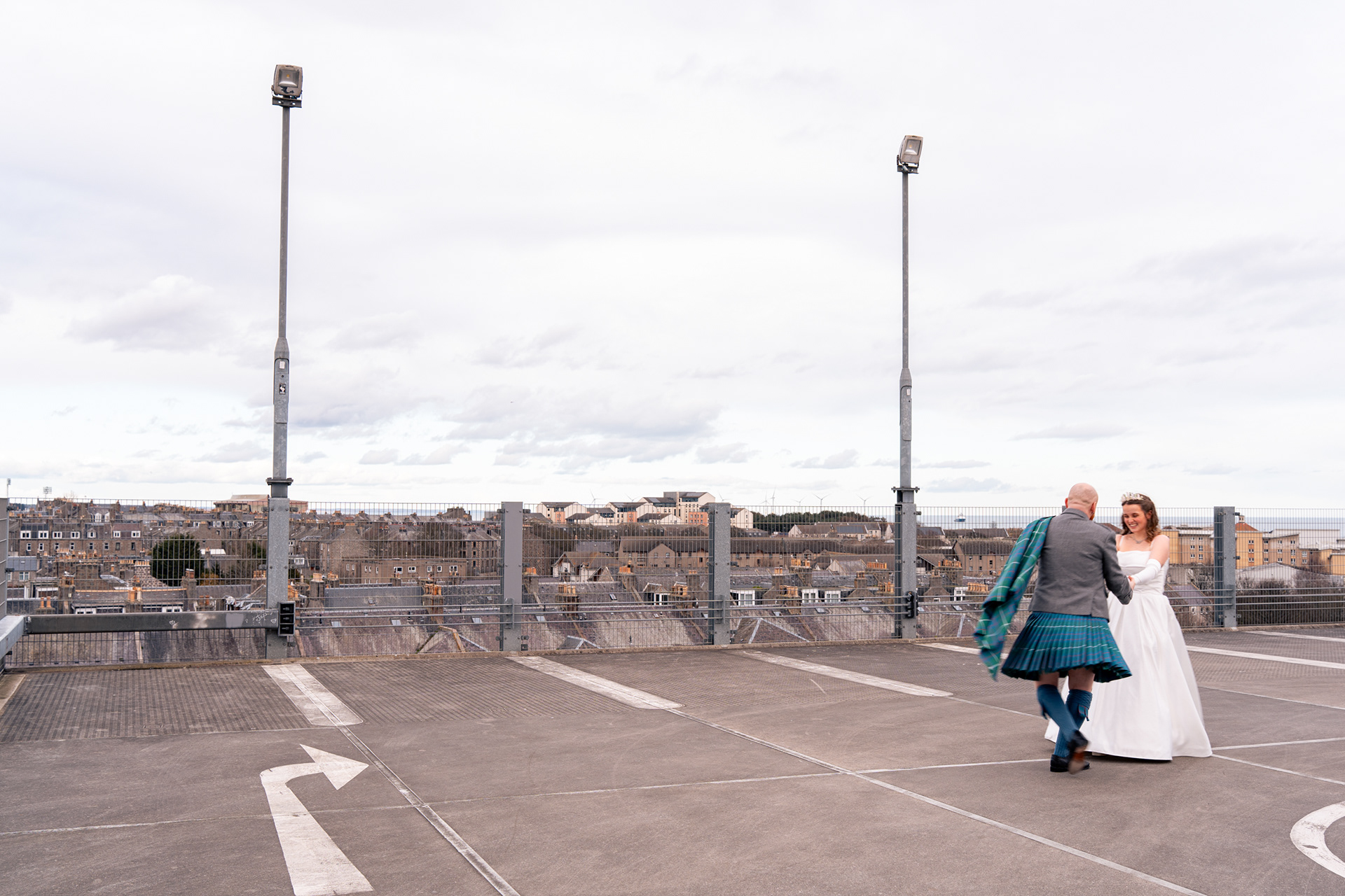 Alternative Aberdeen Wedding Photography: Newlyweds hold hands and laugh as they spin on top of a city centre car park.