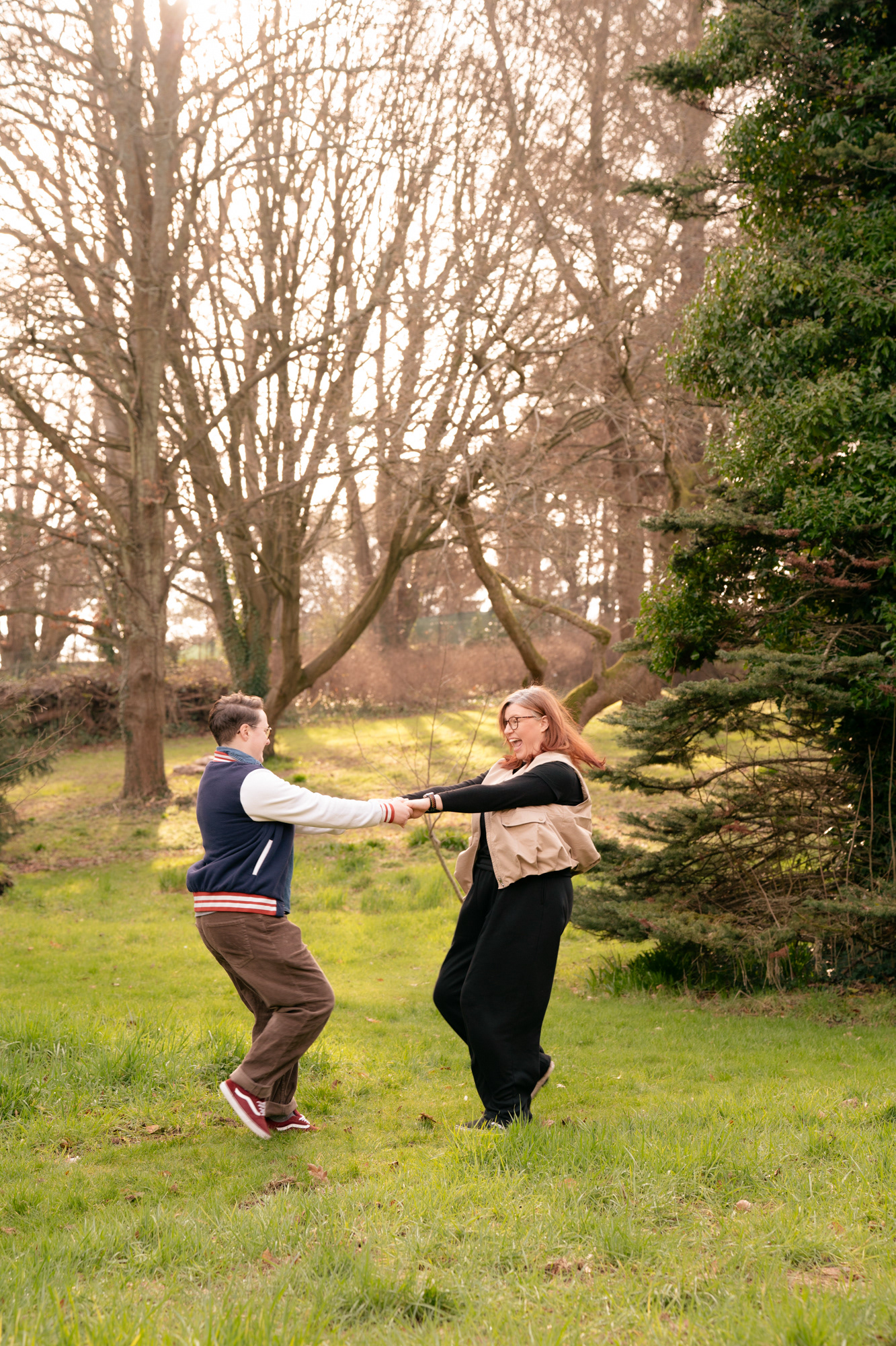 A queer couple (she/her and they/them) hold hands and spin around together