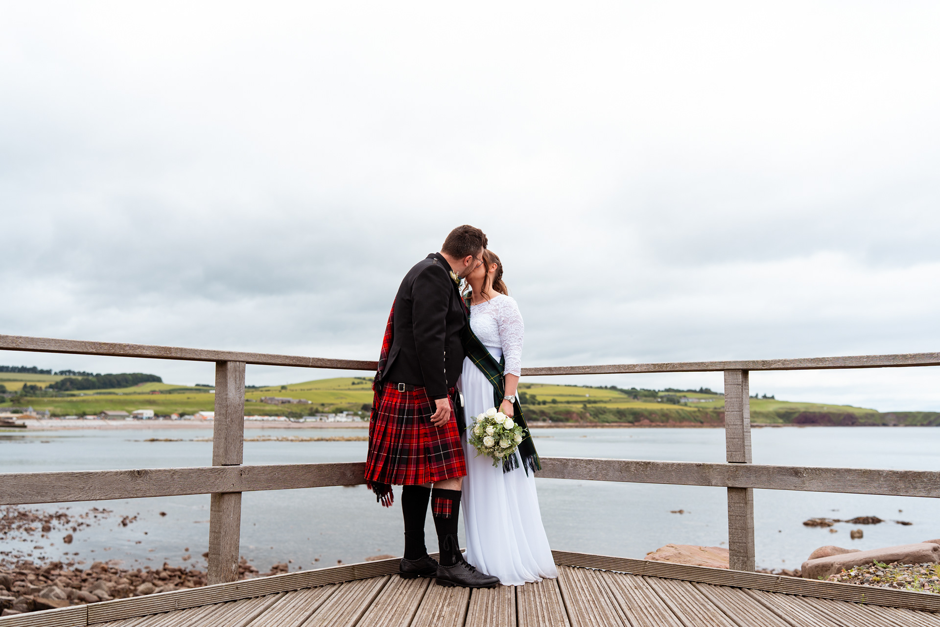 Scottish elopement: Bride and groom kiss against a backdrop of Stonehaven harbour, following their secret registry office wedding.