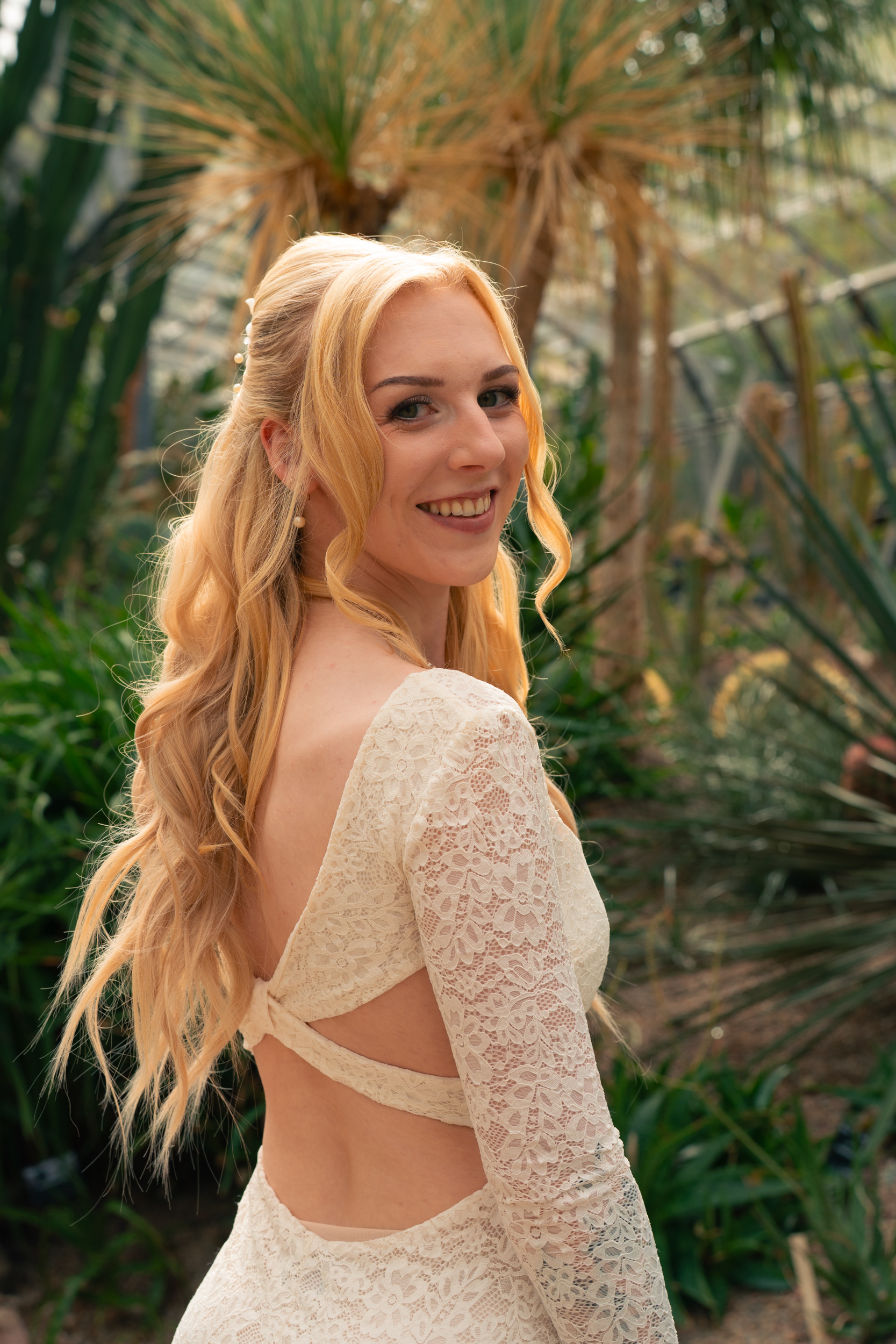 Duthie Park Winter Gardens wedding: Beautiful bride looks back over her shoulder at the camera, backlit by sunlight and surrounded by cactuses.