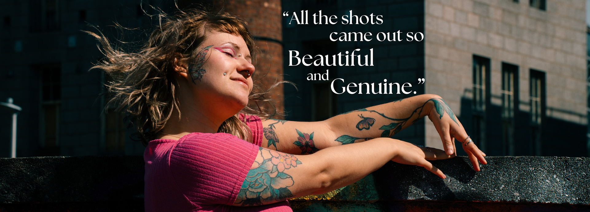 Young woman in pink with tattoos, piercings and short hair blowing in the wind. Review text reads:"All the shots came out so beautiful and genuine."