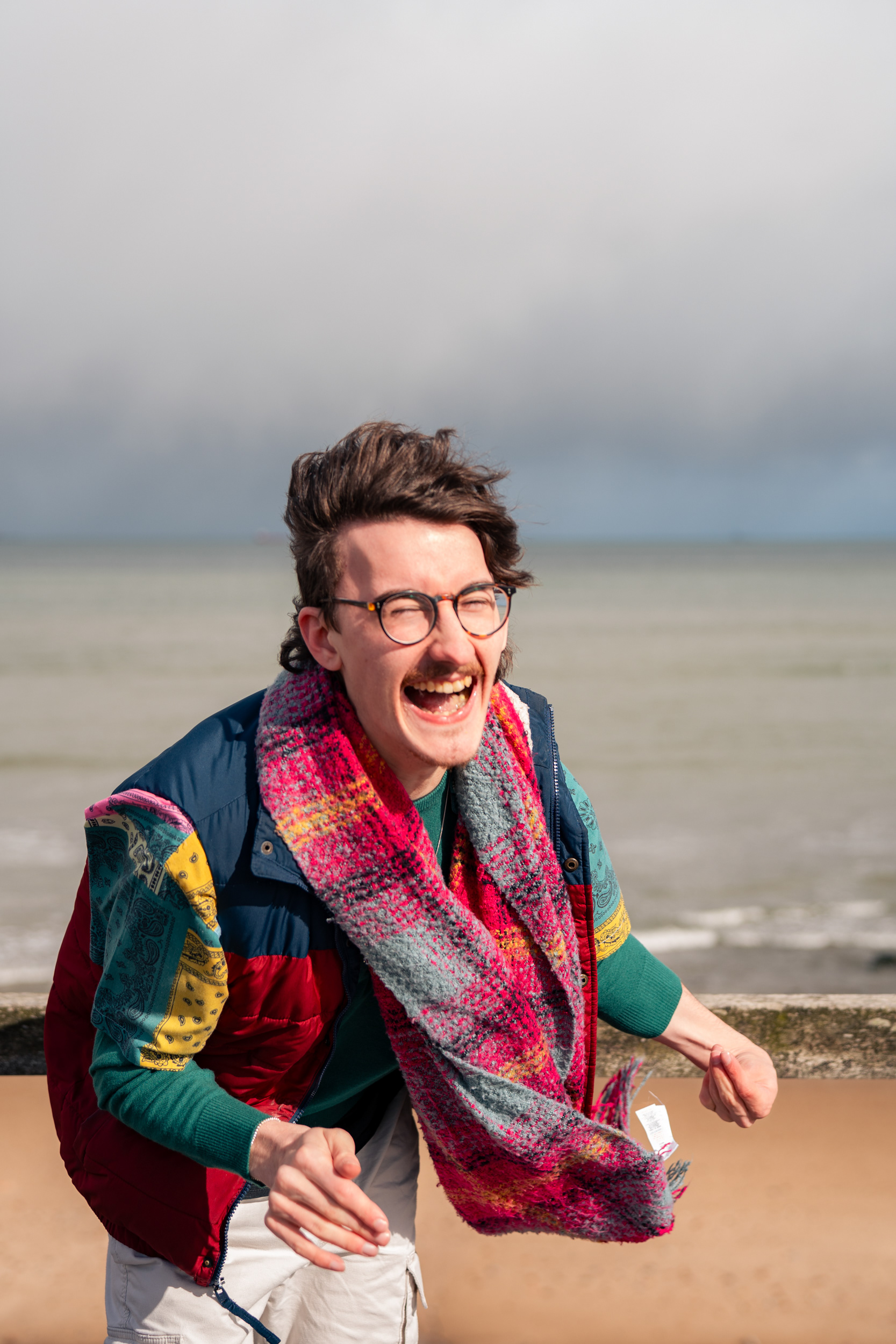 A man in colourful clothes doubles over laughing on Aberdeen beach.