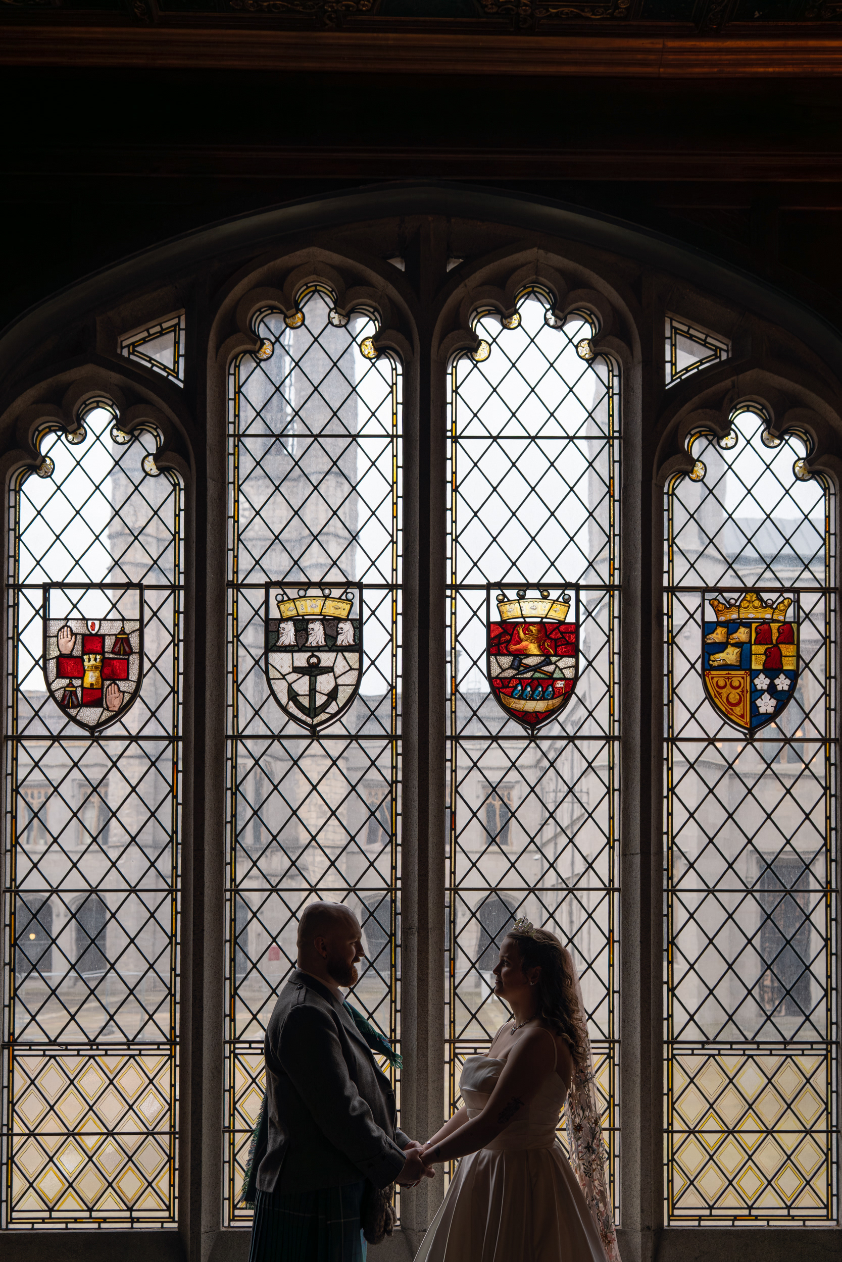 Bride and groom are silhouetted against a stained glass window in Marischal College.