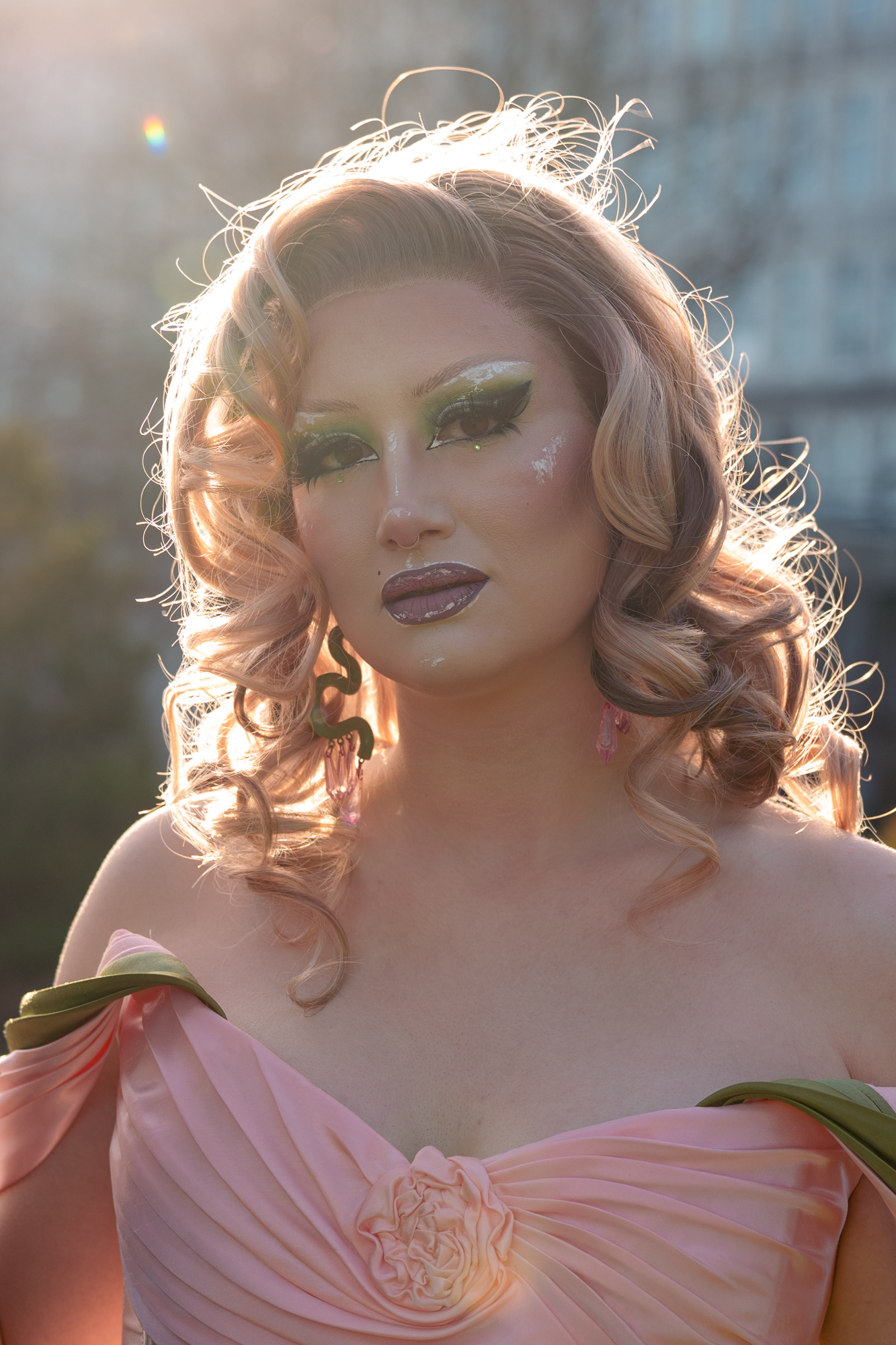 Glamorous head and shoulders shot of a female-to-female drag queen, backlit by the sun.