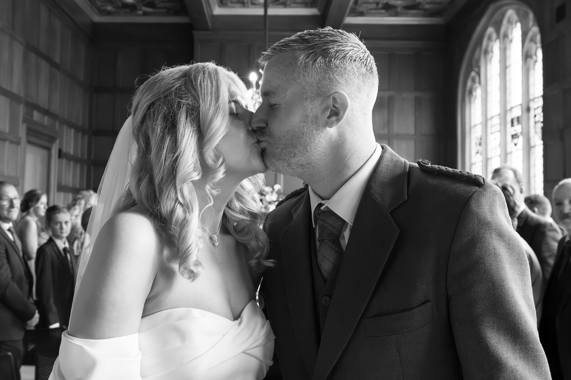Aberdeen registry office wedding: Black and white photo of couple kissing in Marischal College as their guests look on.