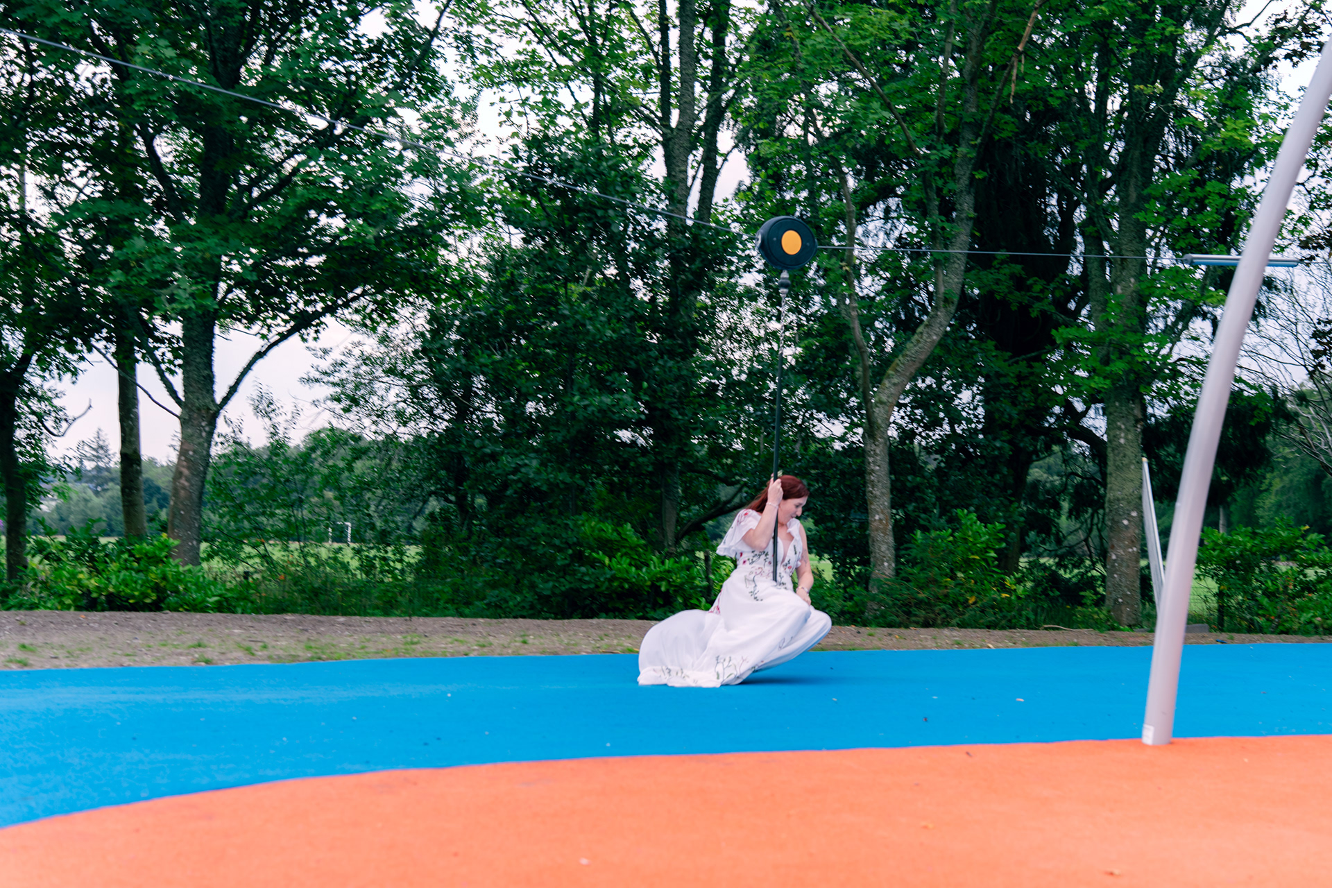 A bride's long white dress swooshes beneath her as she plays on the zip line during her Aberdeen wedding
