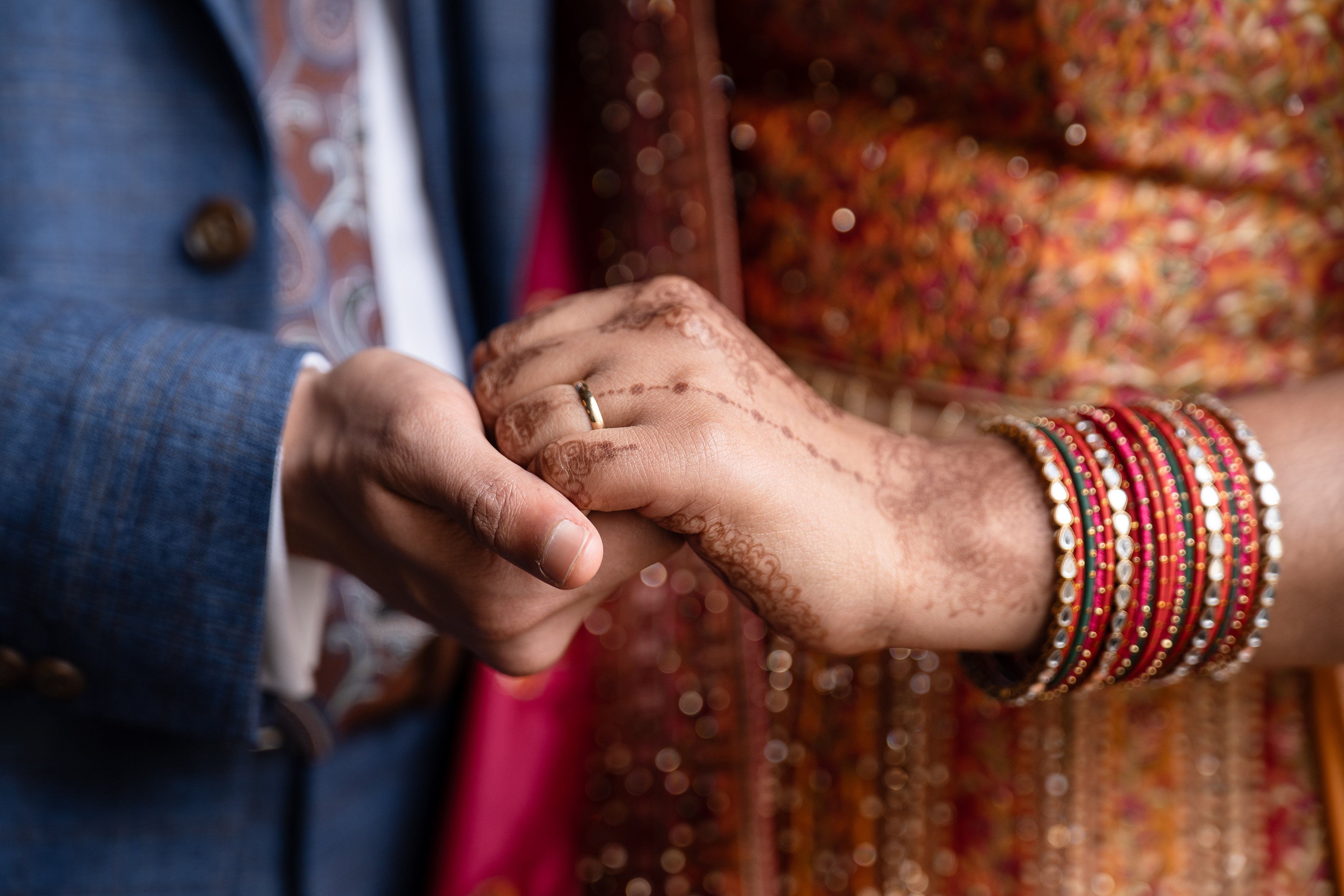 A bride and groom's hands, wedding ring showing. The bride has mehendi and wears multiple bracelets on her arm. Taken at a Marischal College wedding ceremony.