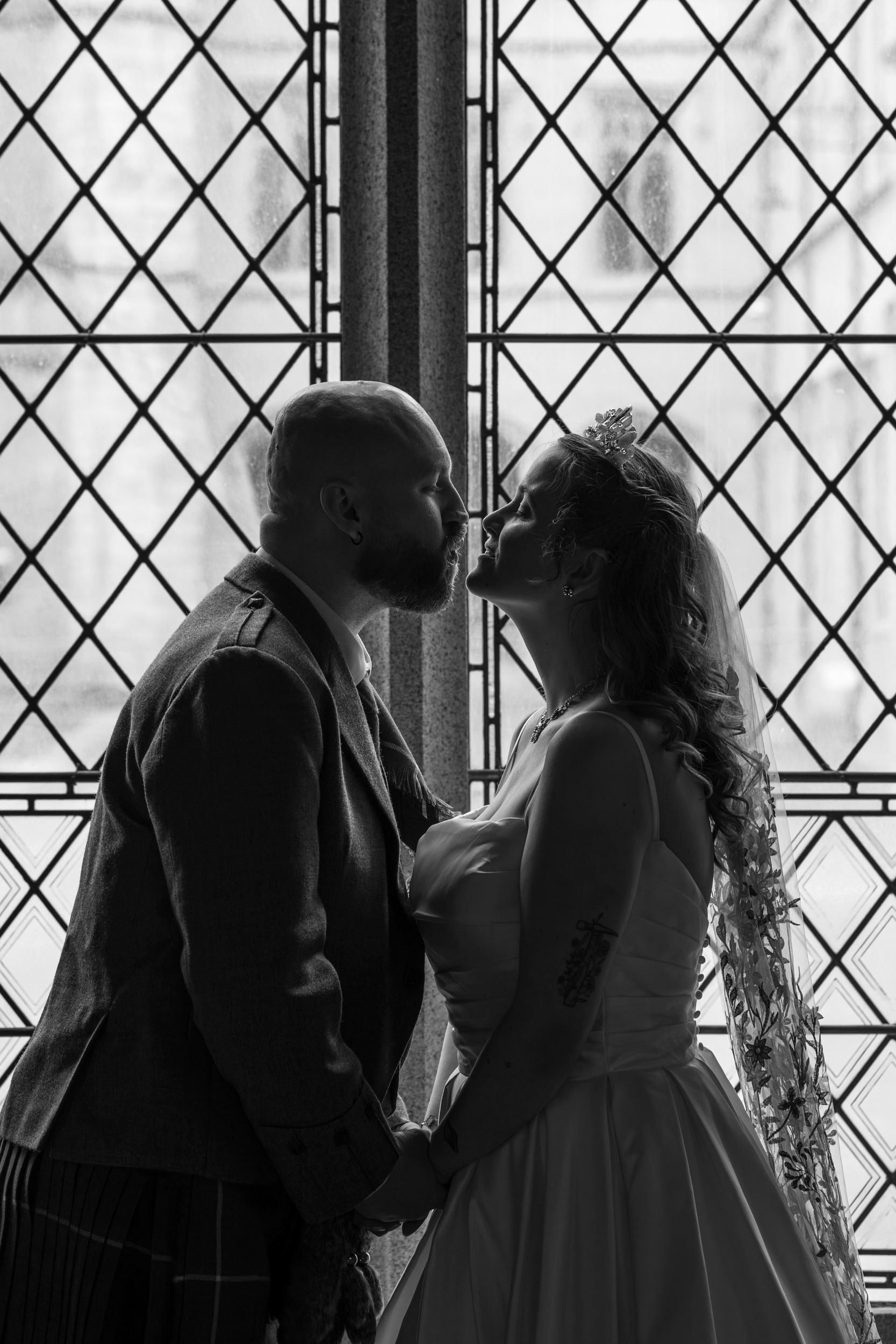Alternative Aberdeen wedding photography: Bride and groom are silhouetted against an ornate window, about to kiss.