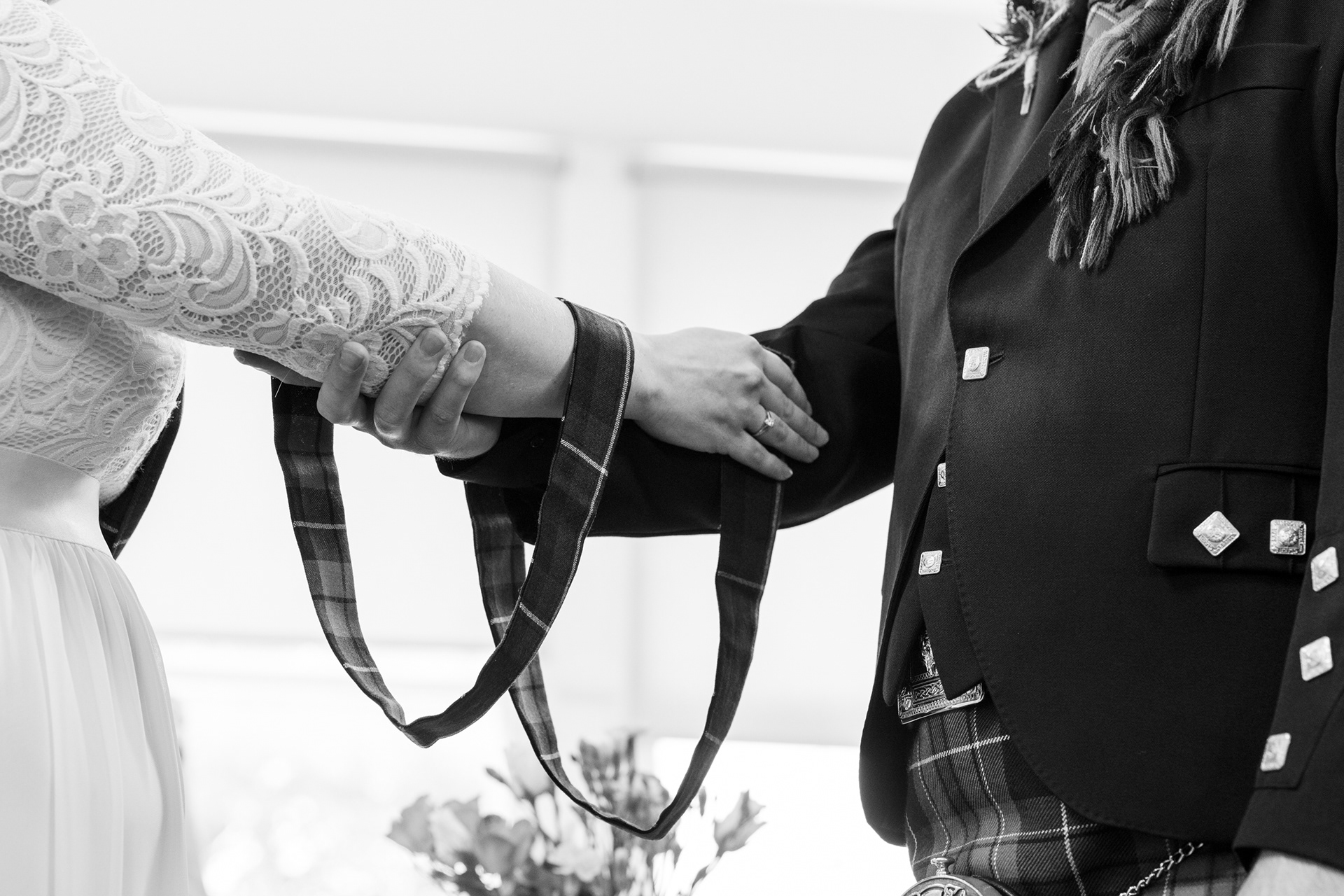 Black and white image of bride and groom's hands with hand fasting cords draped over their wrists.