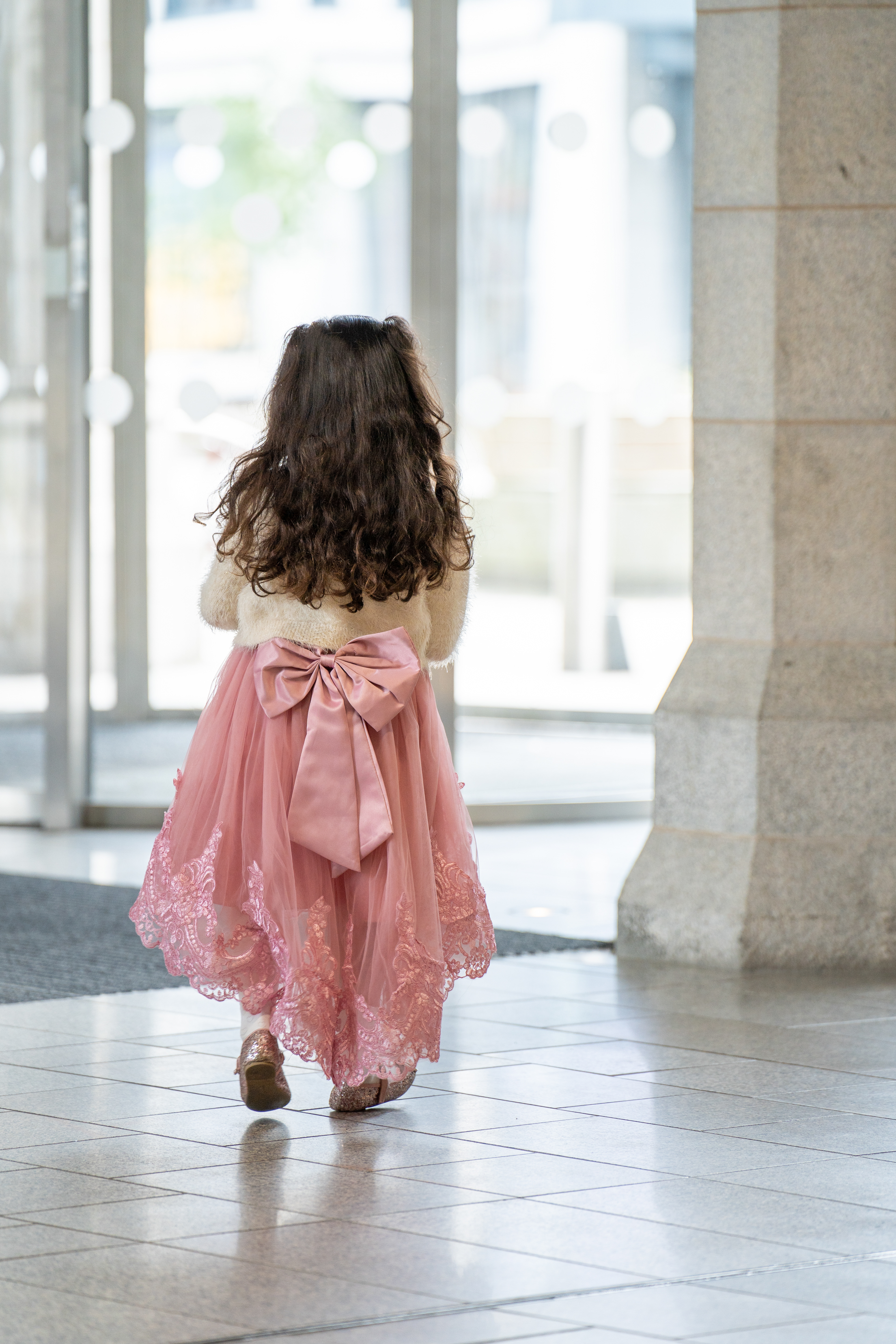 A little girl in a pink party dress is seen from behind, waiting at the entrance of Marischal College.